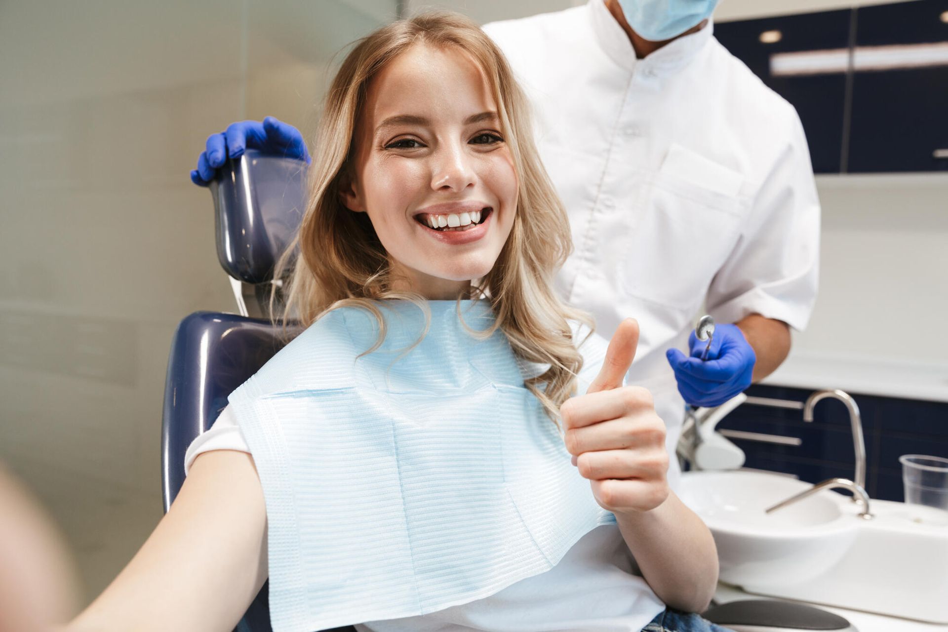 Smiling dental patient giving thumbs up while seated in a dentist chair
