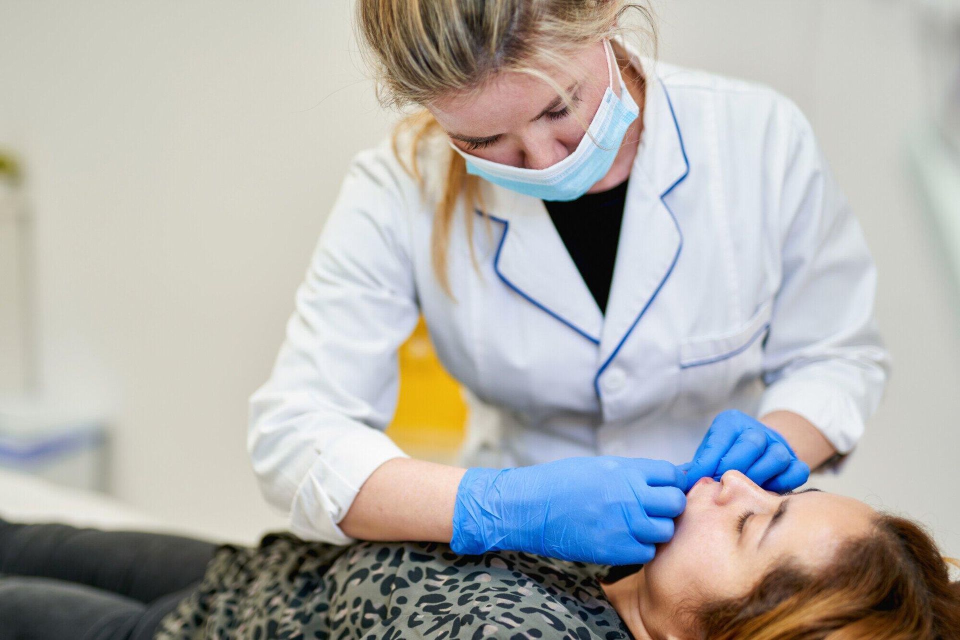 Dentist in white coat and blue gloves examining a patient in a clinic chair