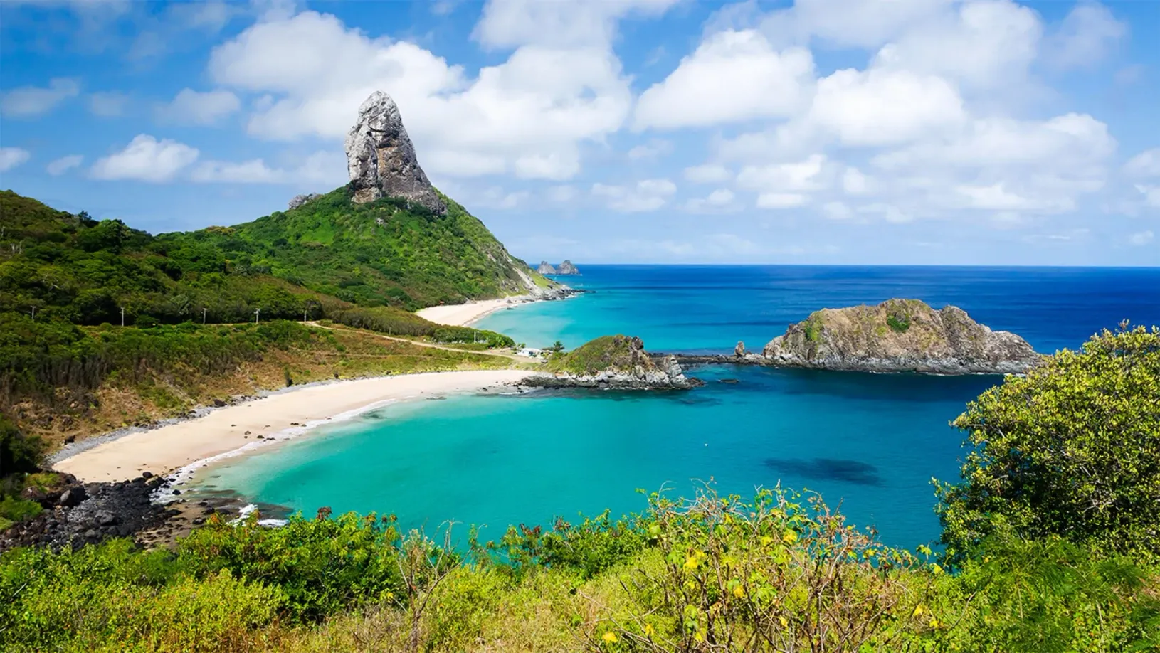 Uma pequena ilha no meio do oceano com uma montanha ao fundo. - Casa Pedrinho Noronha