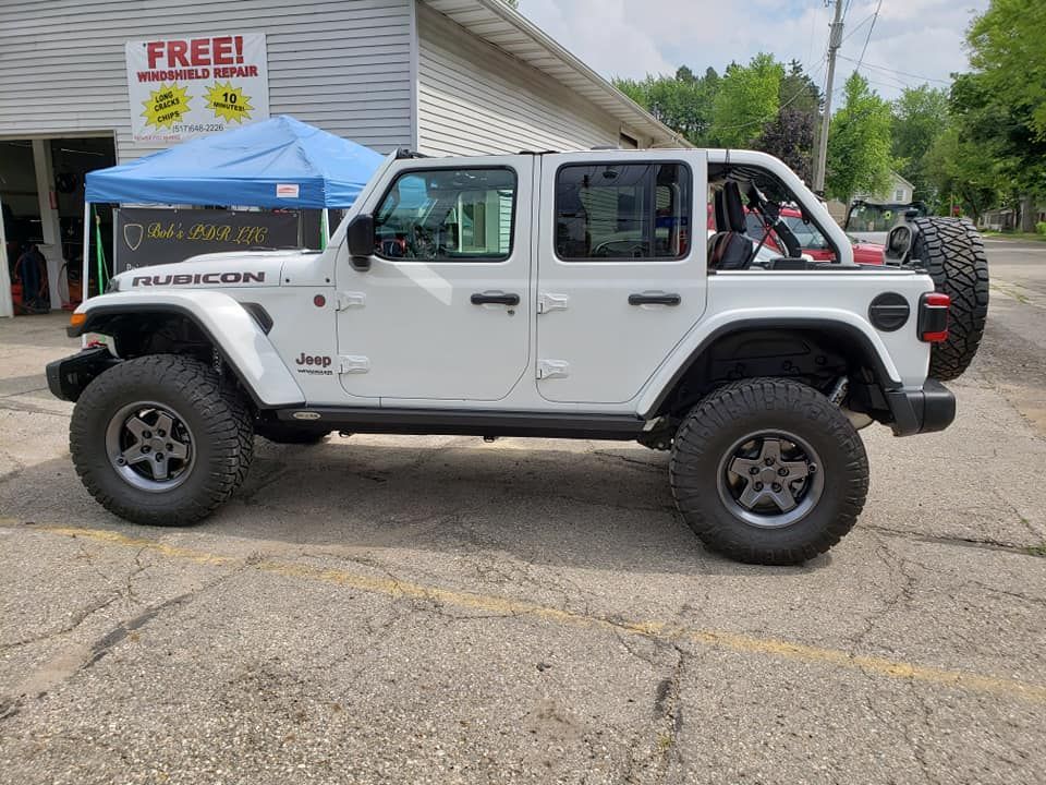 A white jeep wrangler is parked in front of a garage.