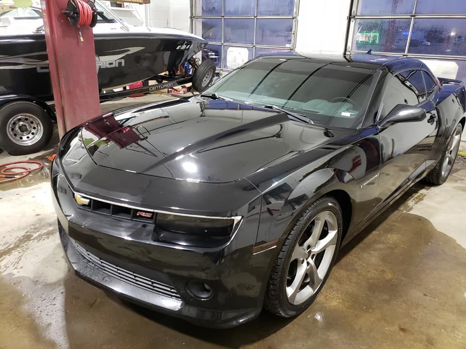 A black car is parked in a garage next to a boat.