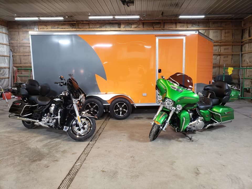 Two motorcycles are parked in front of an orange trailer in a garage.