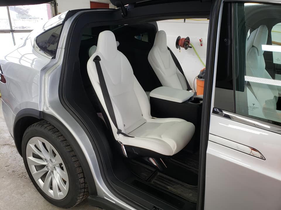 The back seat of a silver tesla model x with the door open.