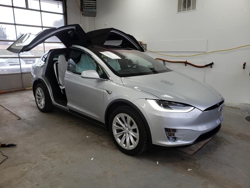 A silver tesla model x is parked in a garage with its doors open.