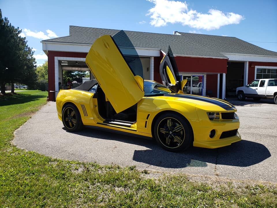 A yellow sports car with its doors open is parked in front of a garage.