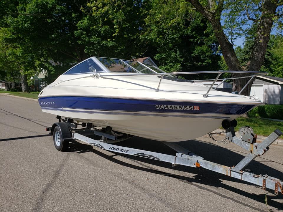 A white and blue boat is parked on a trailer on the side of the road.
