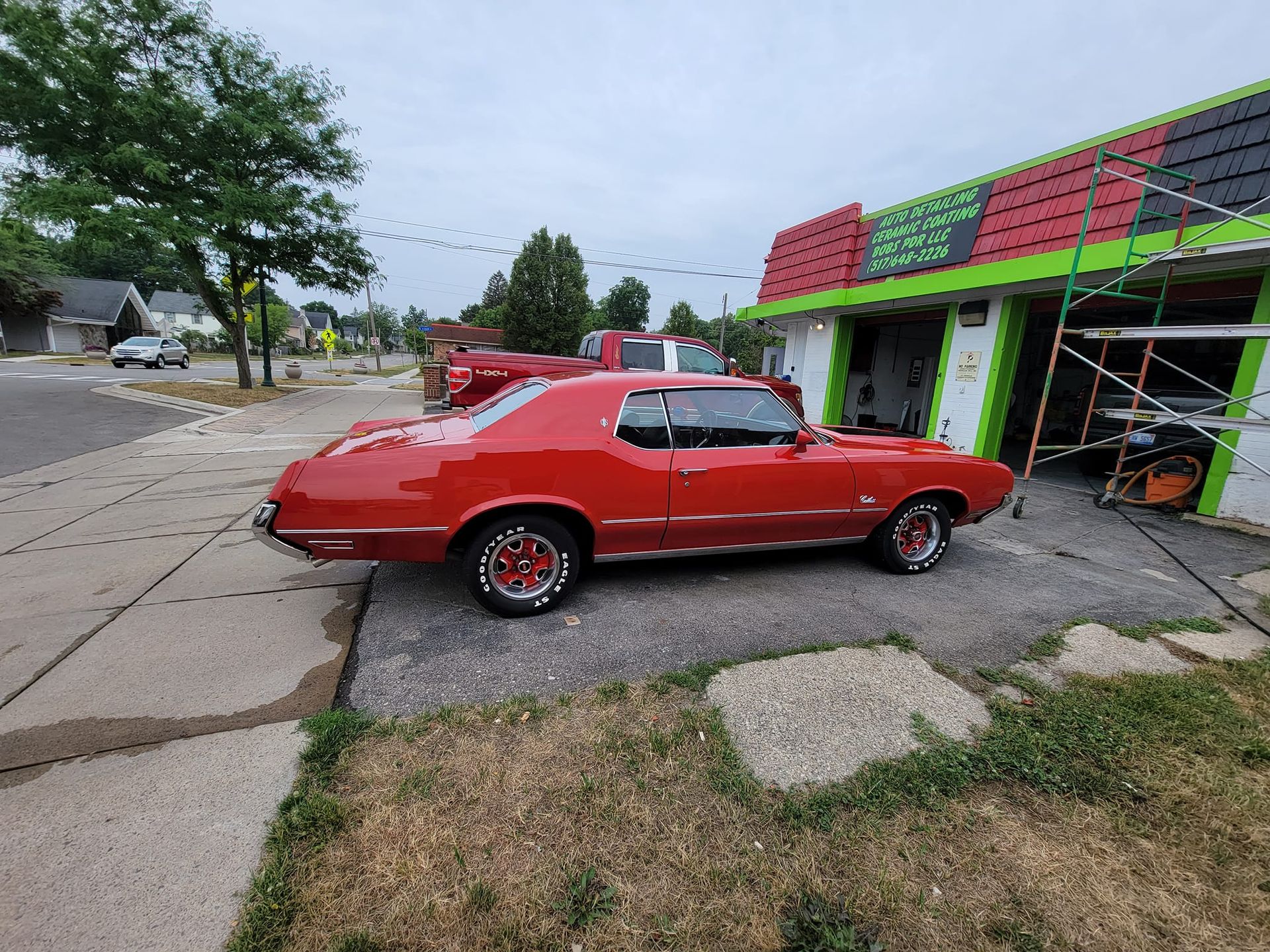 A red car is parked in front of a green and red building.