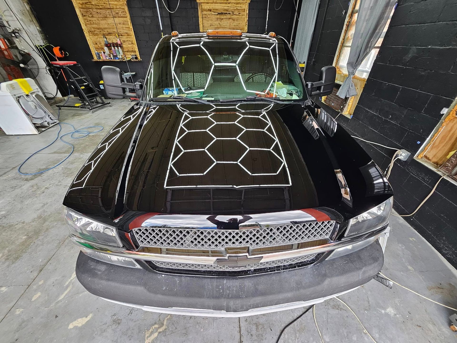 A black truck with a honeycomb design on the hood is parked in a garage.
