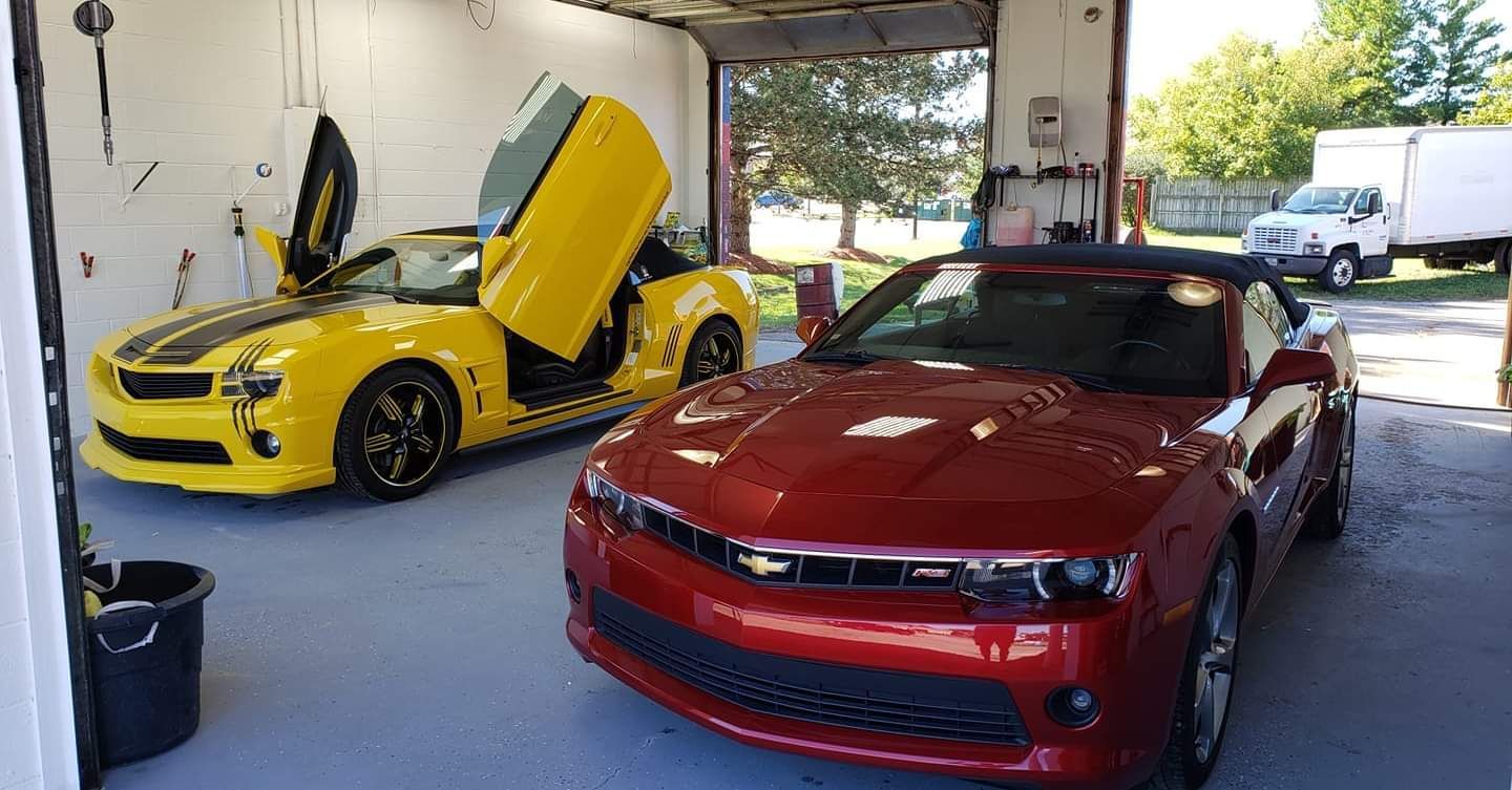 A yellow car and a red car are parked in a garage.