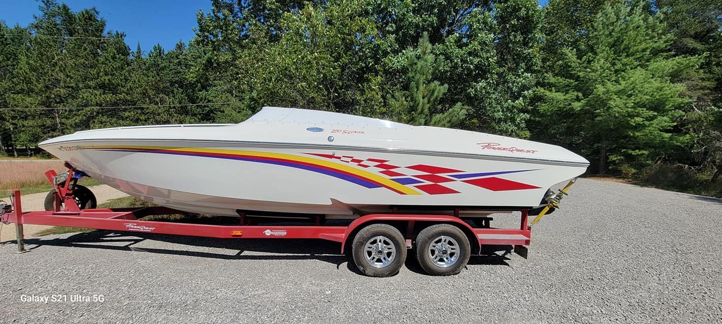 A speed boat is parked on a trailer in a gravel lot.