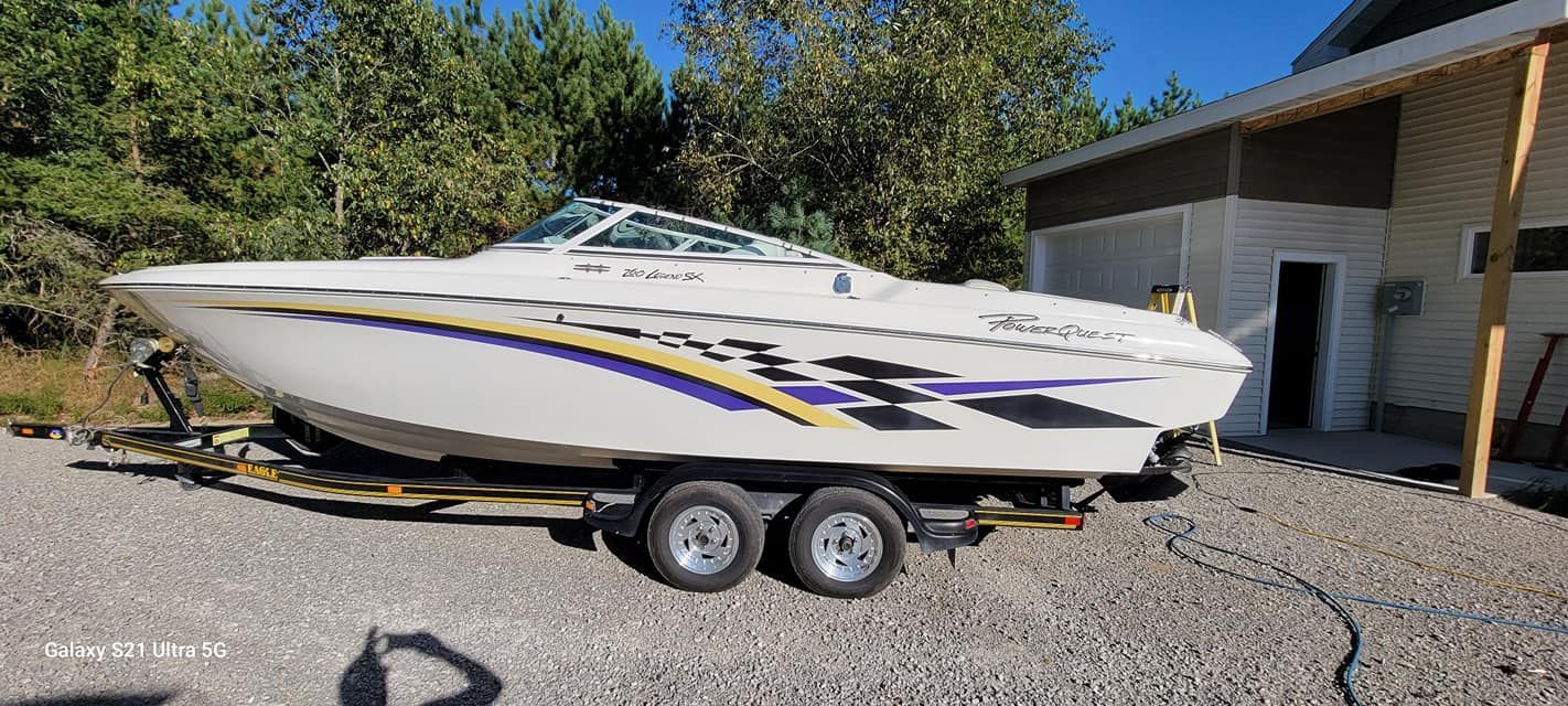 A white boat is parked on a trailer in front of a house.