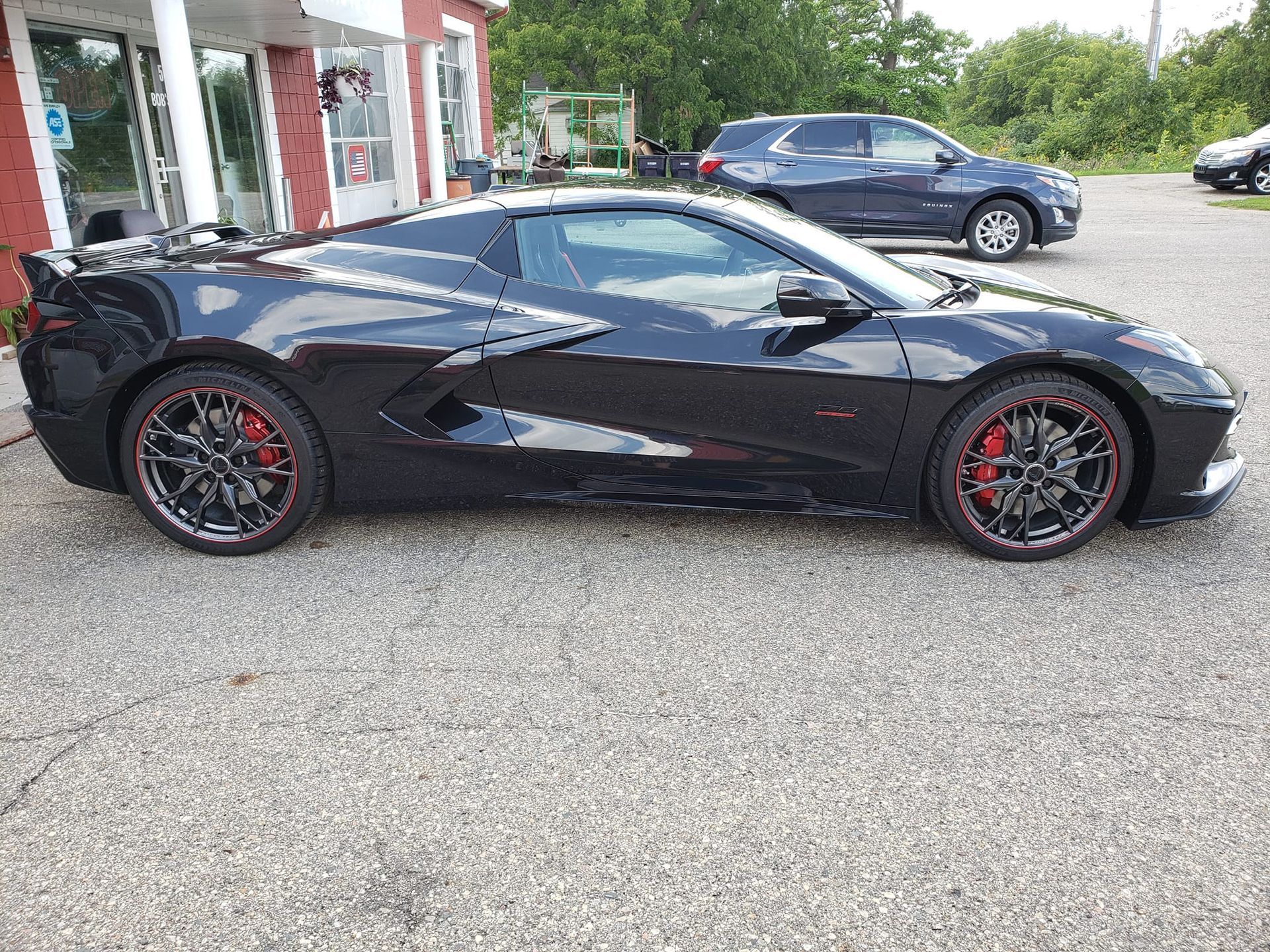 A black sports car is parked in a gravel lot in front of a building.
