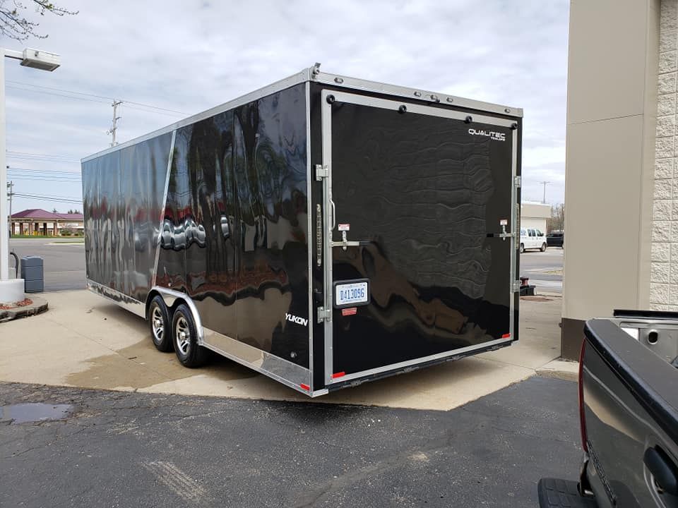 A black trailer is parked in a parking lot next to a truck.