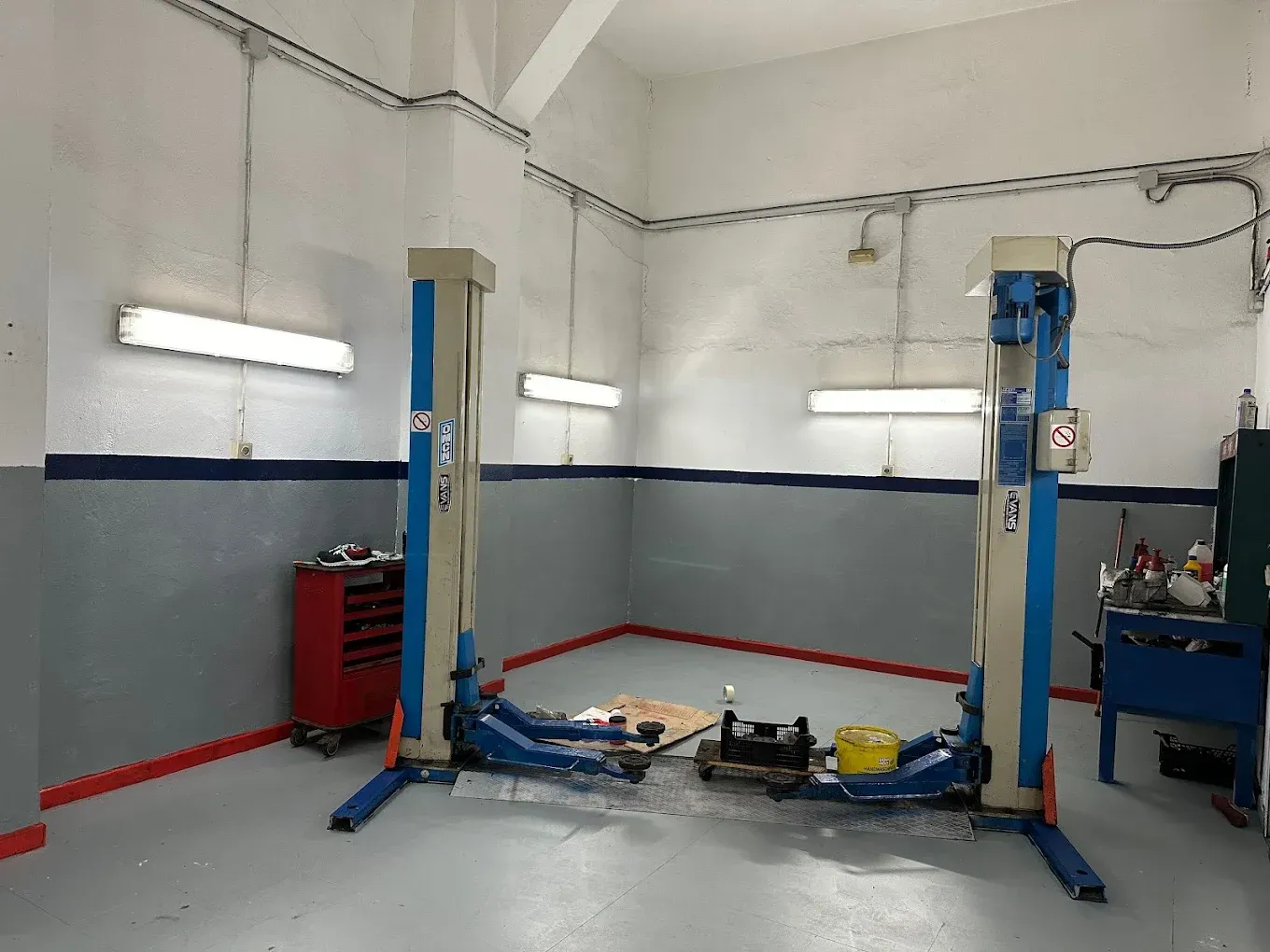Interior de un taller de reparación de automóviles con dos elevadores de vehículos, herramientas y bancos de trabajo.
