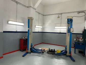 Interior de un taller de reparación de automóviles con dos elevadores de vehículos, herramientas y bancos de trabajo.