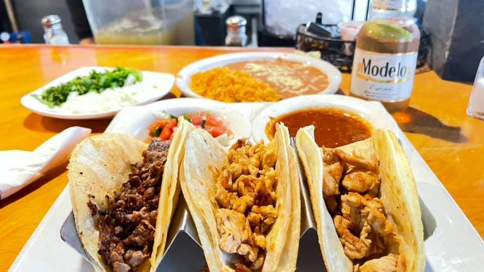 Three tacos are sitting on a white plate on a wooden table.