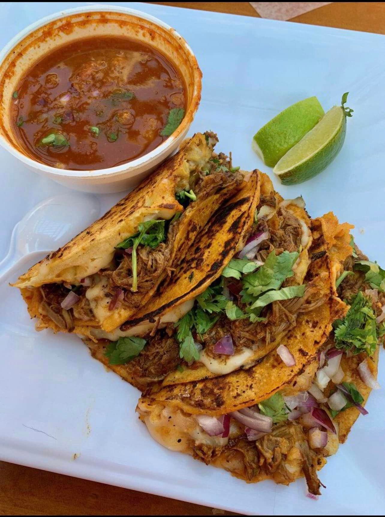 A white plate topped with tacos and a bowl of soup.