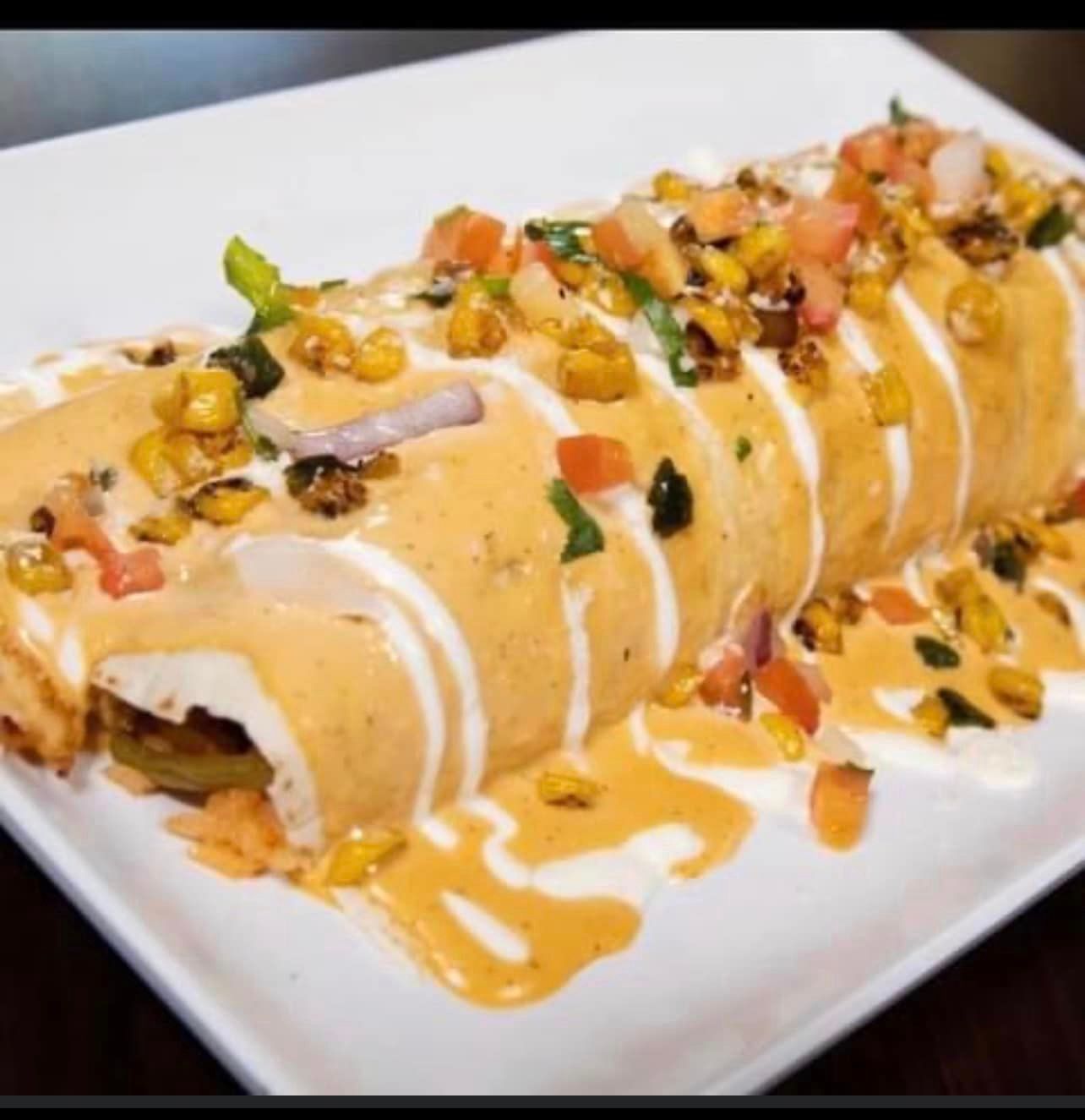 A burrito with sauce and vegetables on a white plate