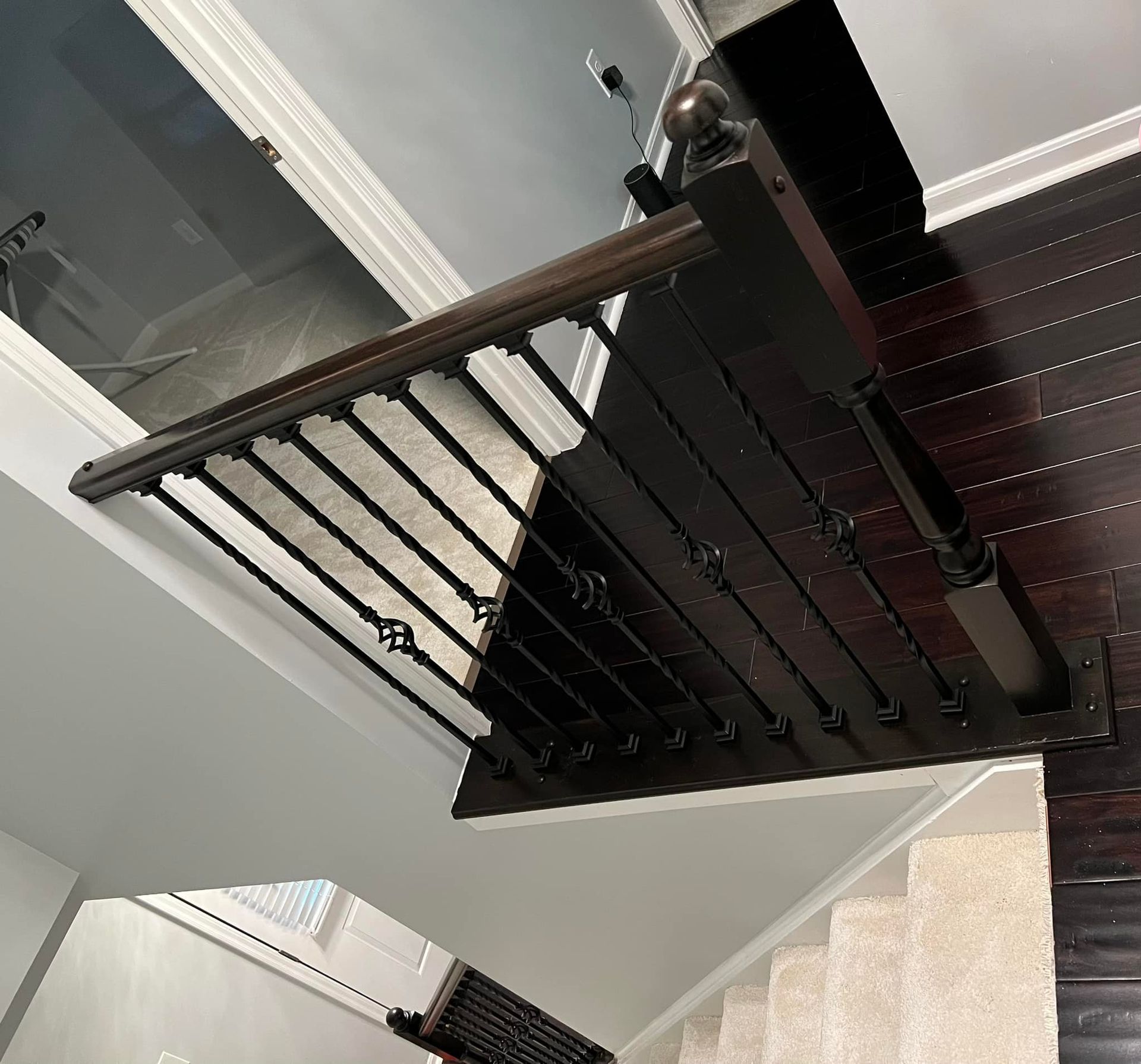 Dark wooden stair railing with black iron spindles, viewed from above.
