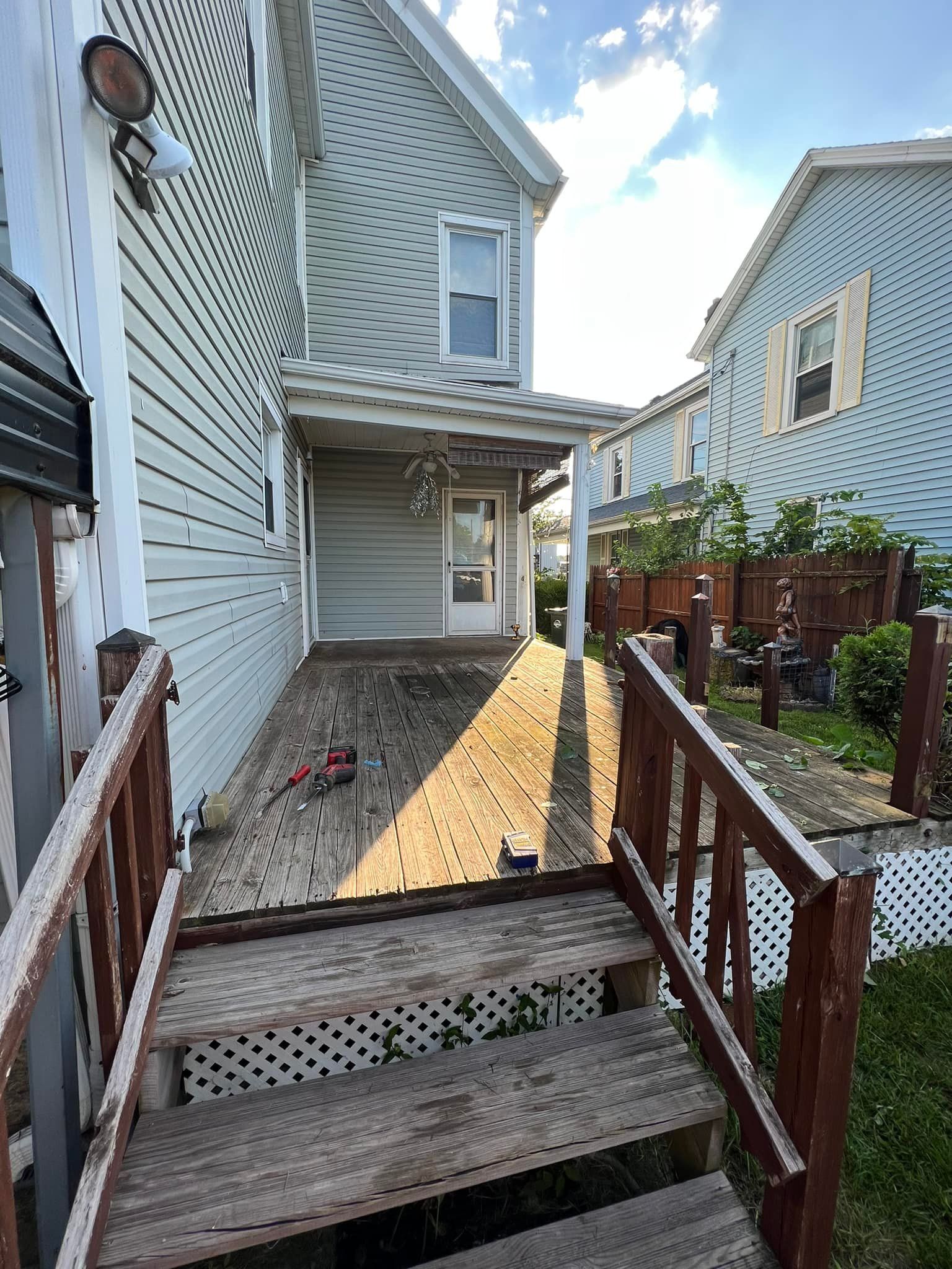 Wooden deck leading to a covered porch on a house; adjacent buildings and fences.
