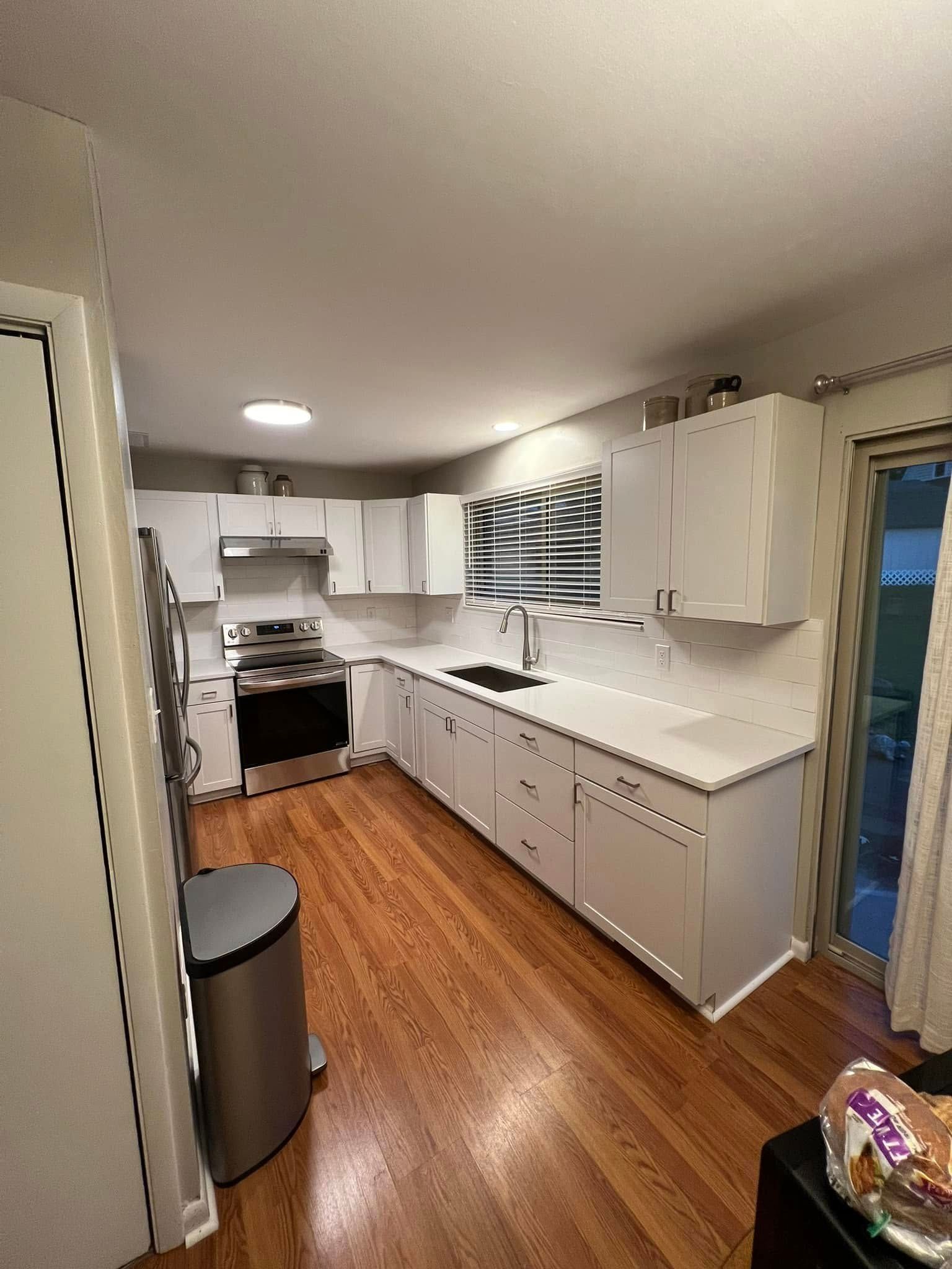 White kitchen with stainless steel appliances, white countertops, and wood floors.