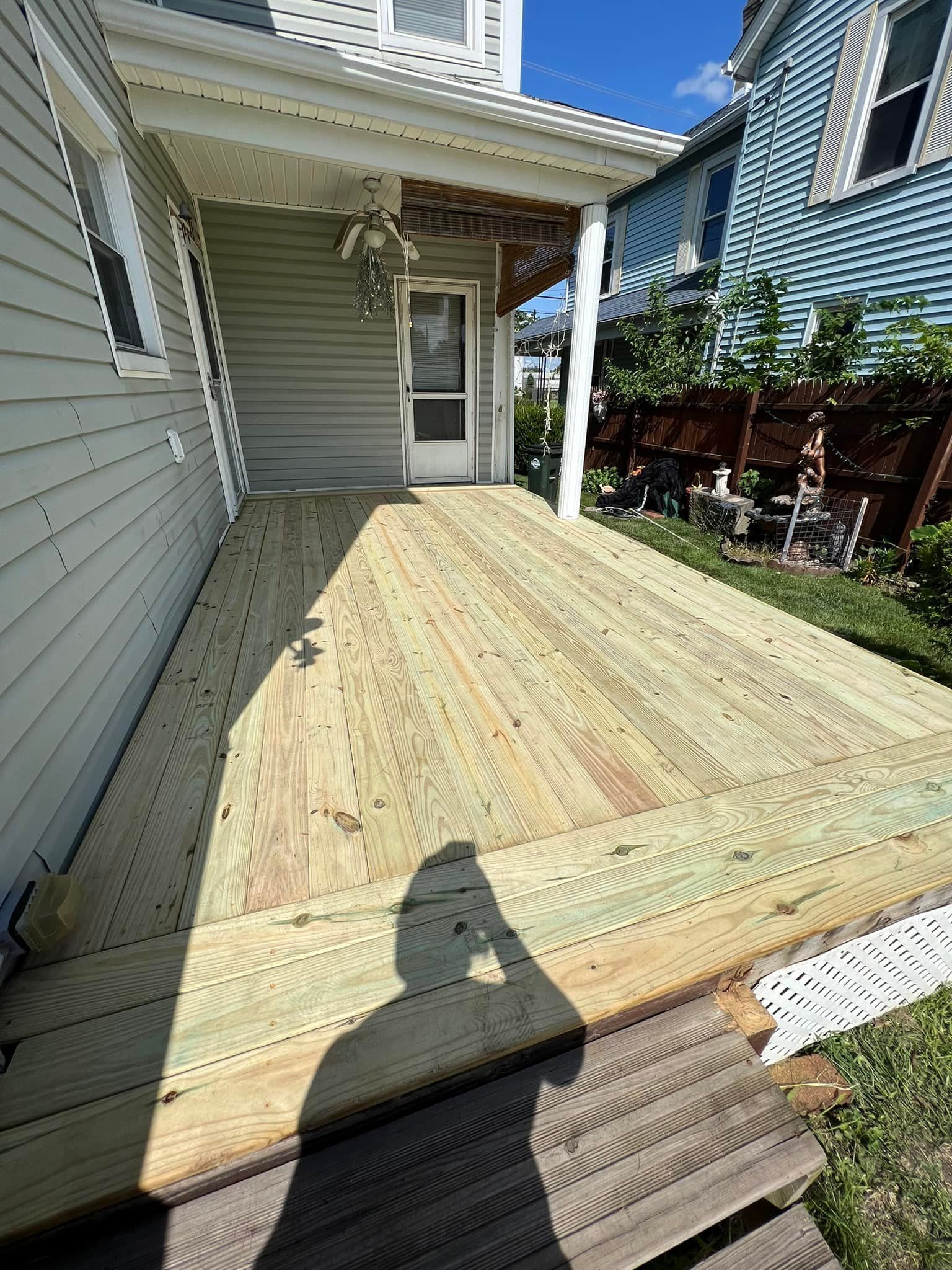 Newly built wooden deck attached to a gray house, with a porch overhang and green grass.