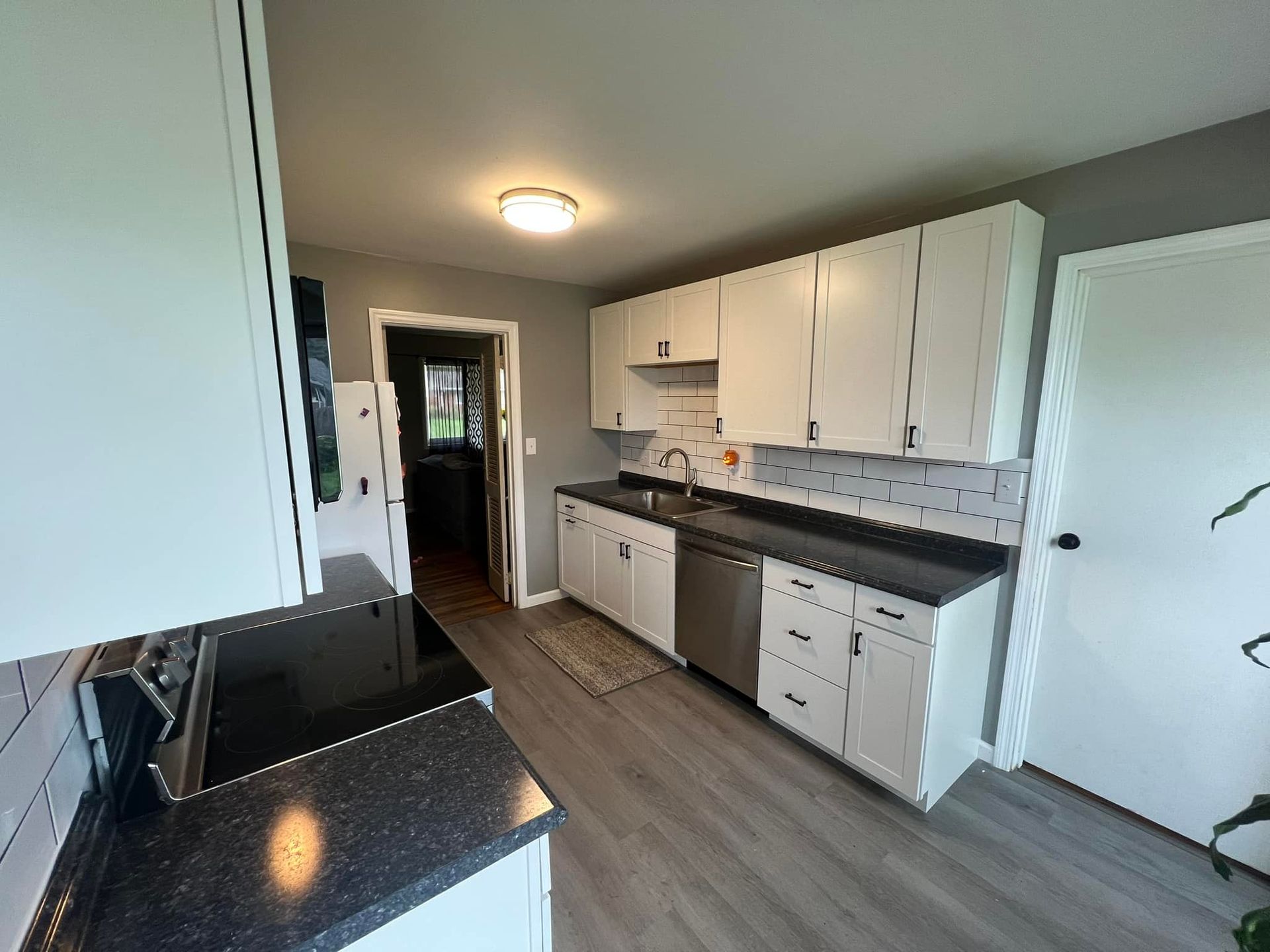 White kitchen cabinets, black countertops, stainless steel appliances, and gray flooring.