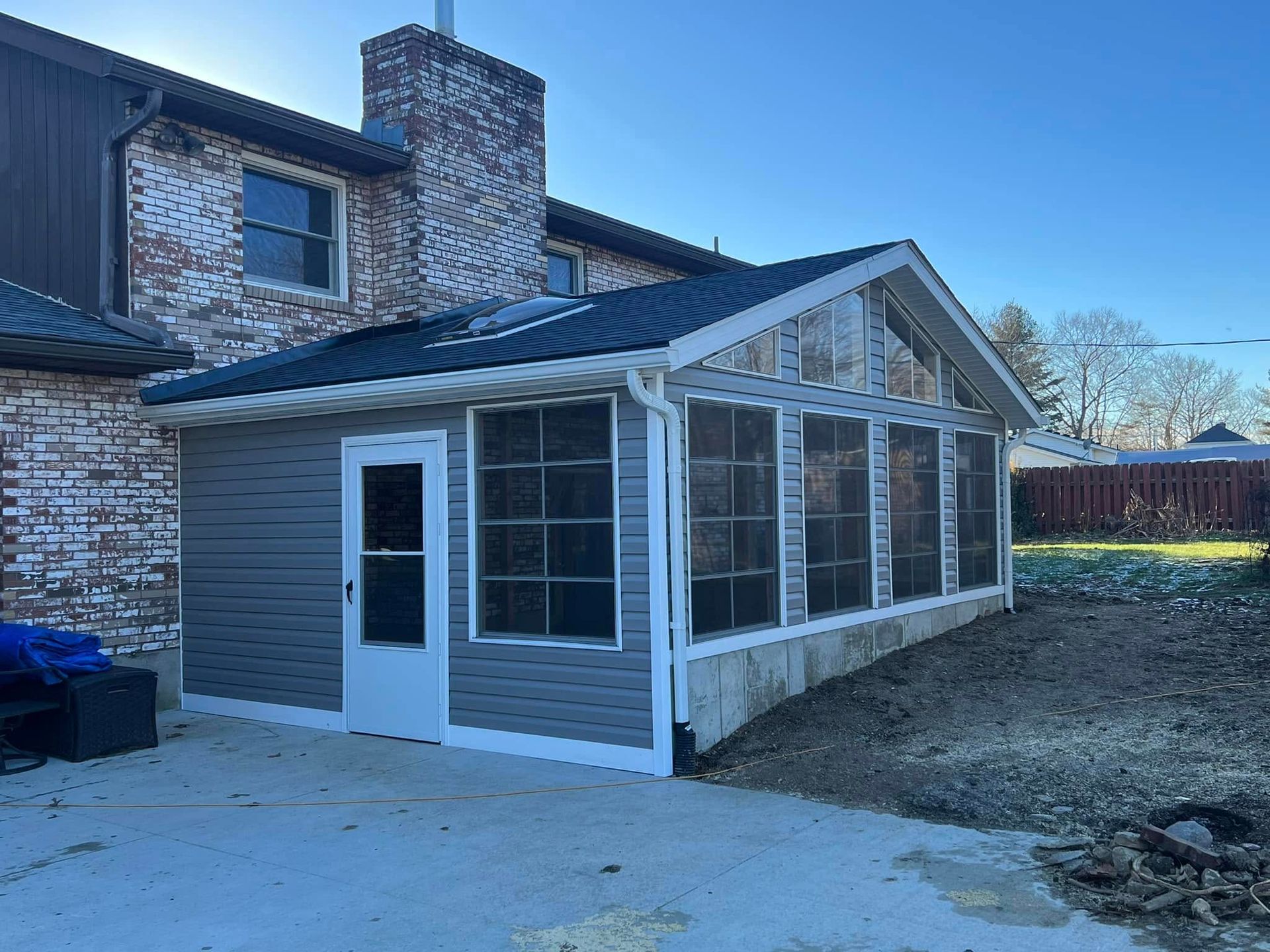 A newly constructed screen porch attached to a brick house with gray siding.