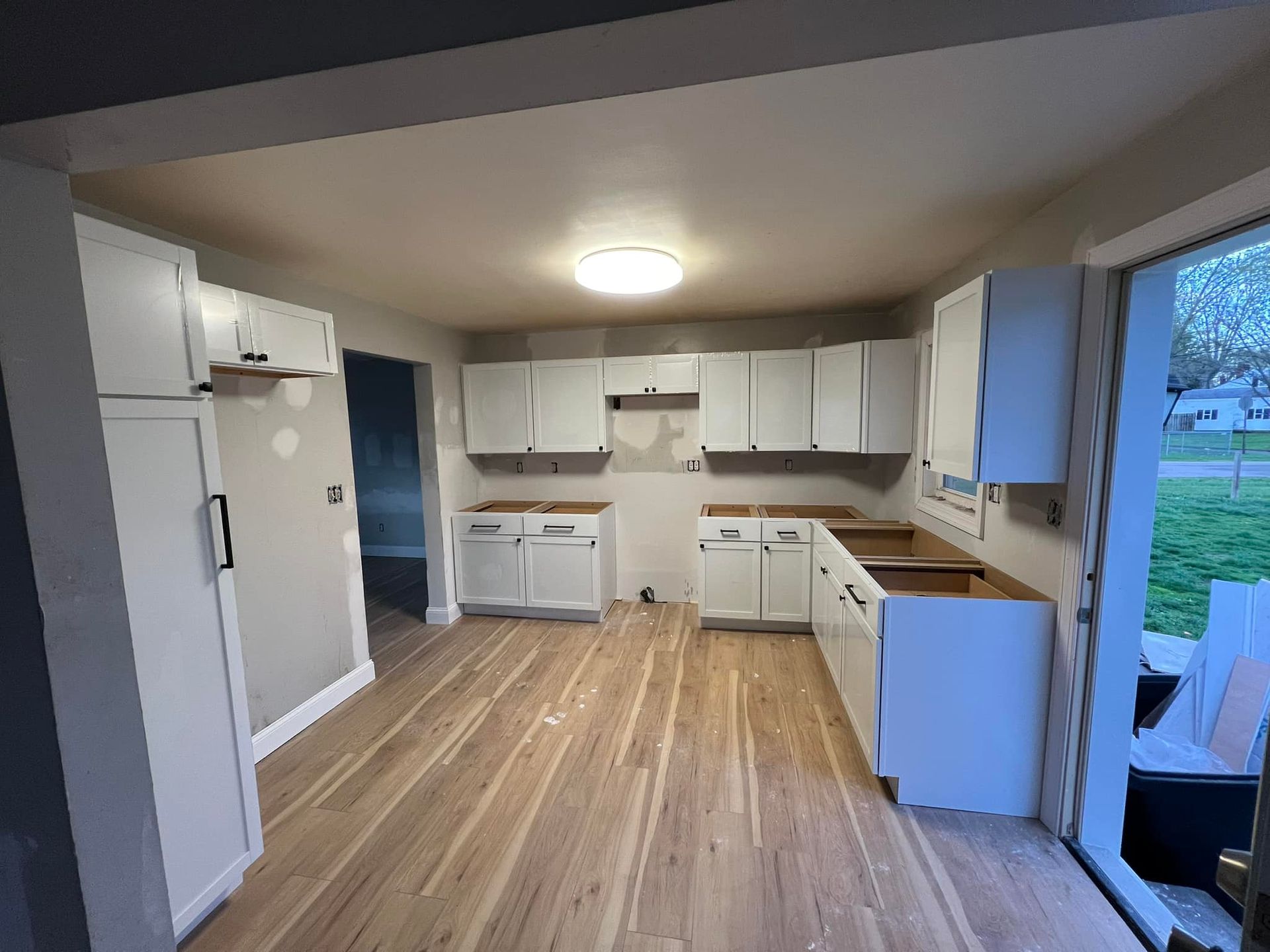 Kitchen renovation in progress: white cabinets, light wood floor, open doorway, neutral walls.