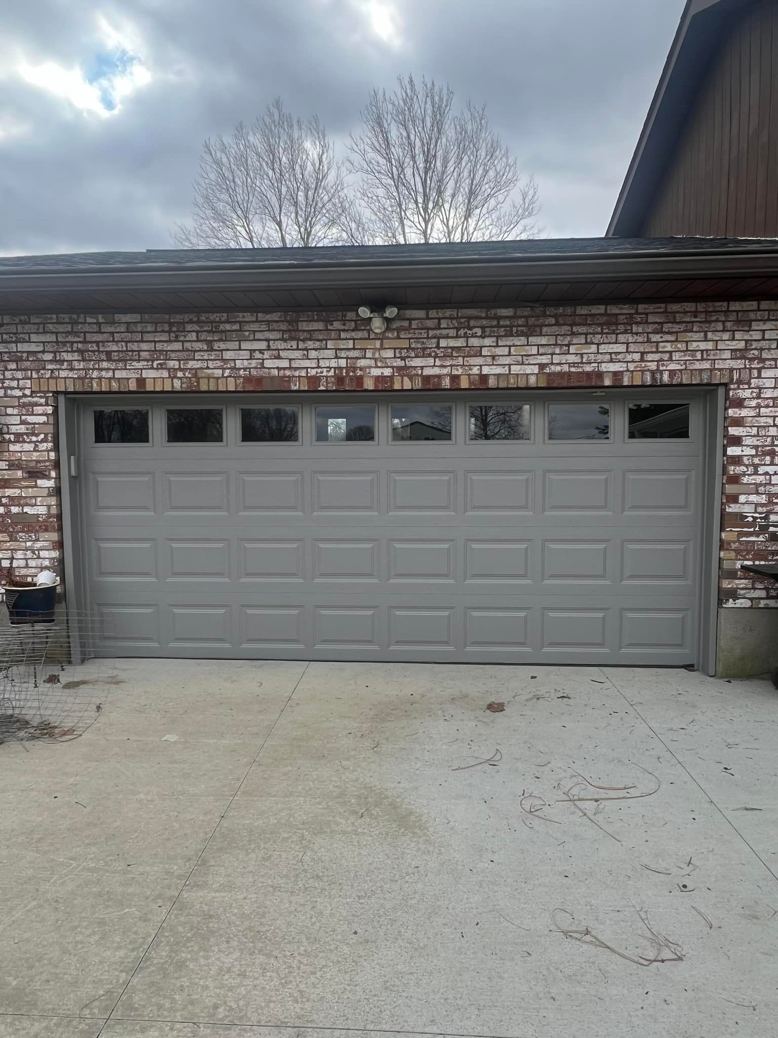 Gray garage door on a brick building with overcast sky in the background.