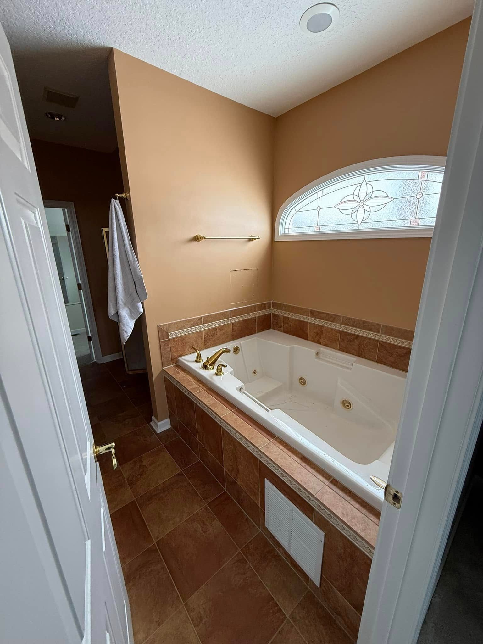 Bathroom with a jacuzzi tub, brown tile, and tan walls.