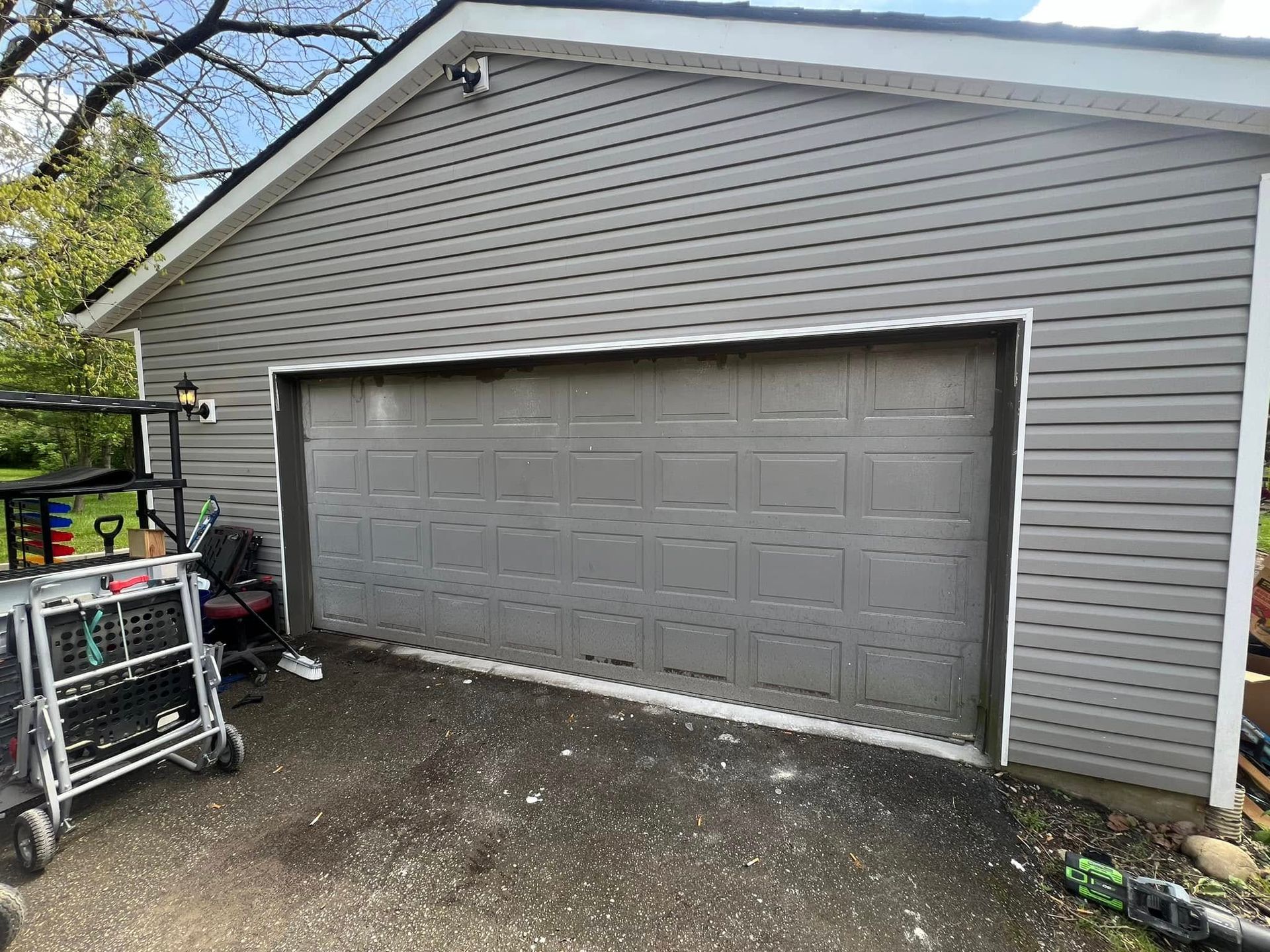 Grey garage with grey door, grey siding, and white trim. Work table and tools nearby.