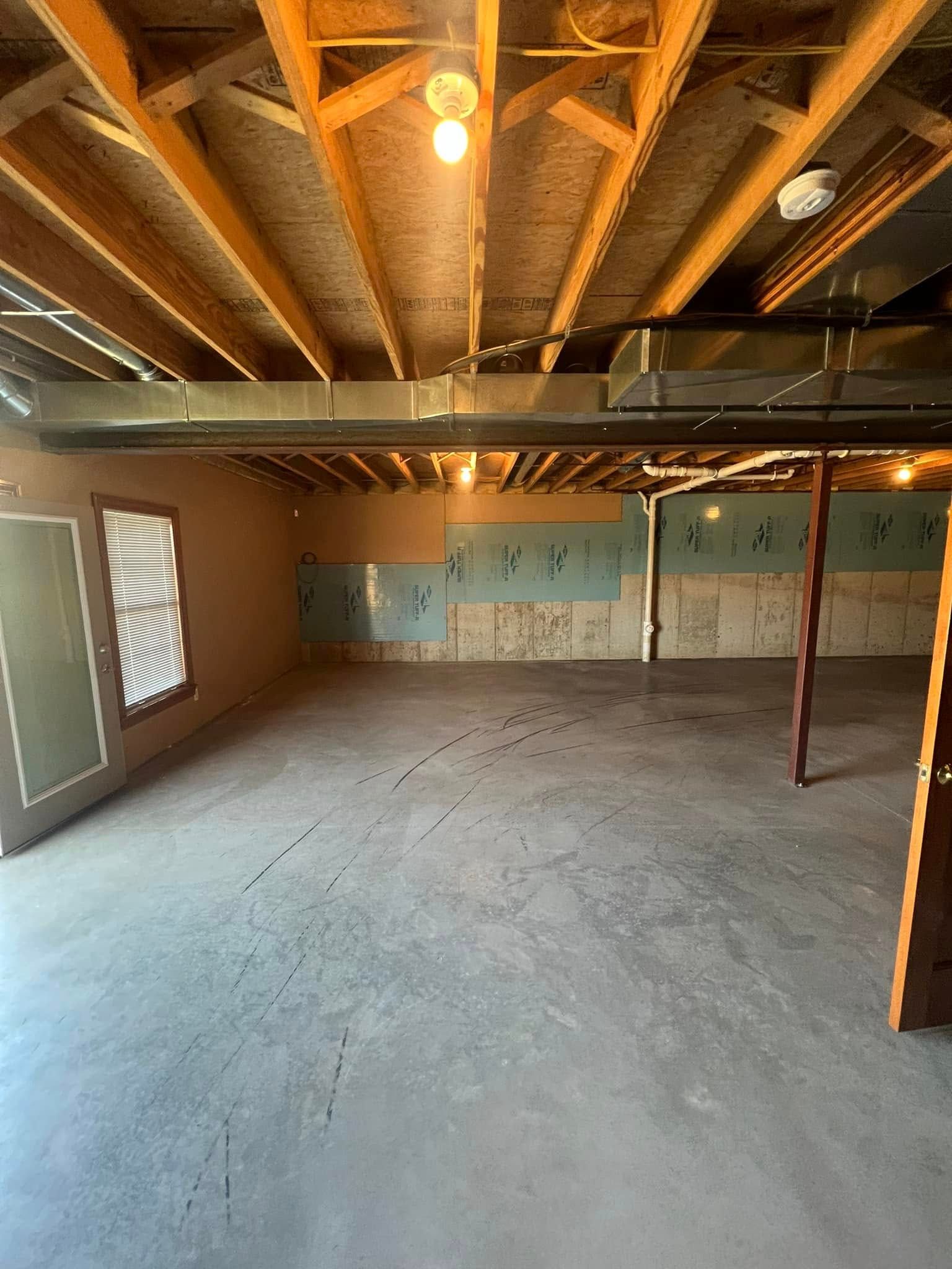 Empty unfinished basement with concrete floor, exposed ceiling beams, and ductwork.