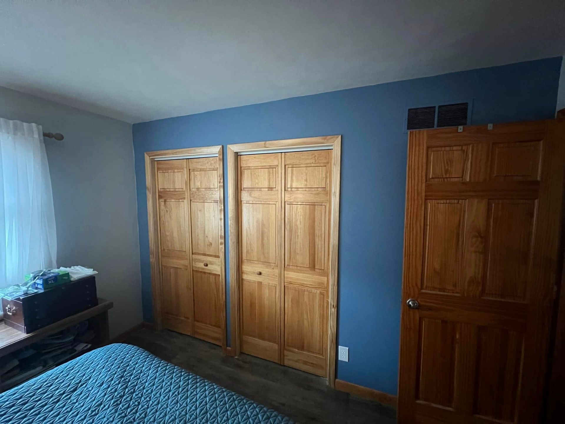 Bedroom with blue wall, wooden closet doors, and a bed with a blue cover.