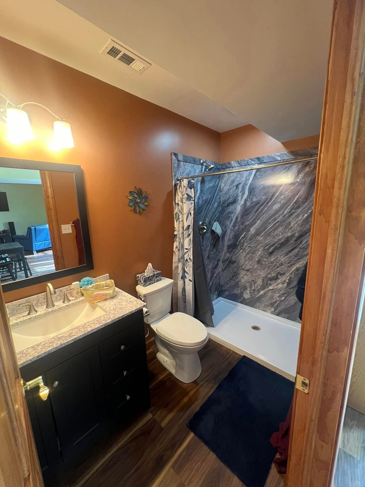 Bathroom with dark brown walls, black vanity, and marble-patterned shower.