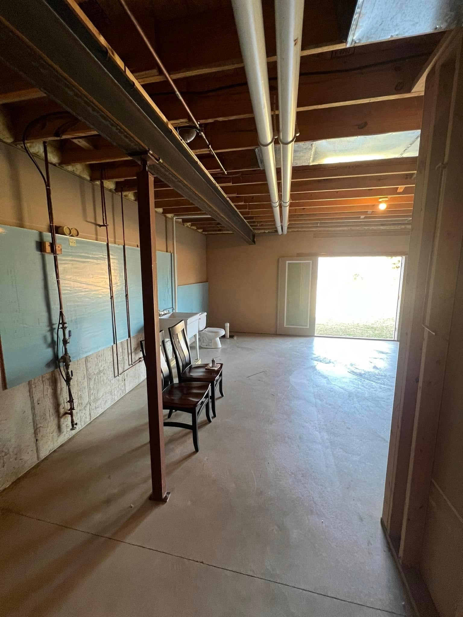 Basement interior with concrete floor, wood beams, support post, and door to outside.