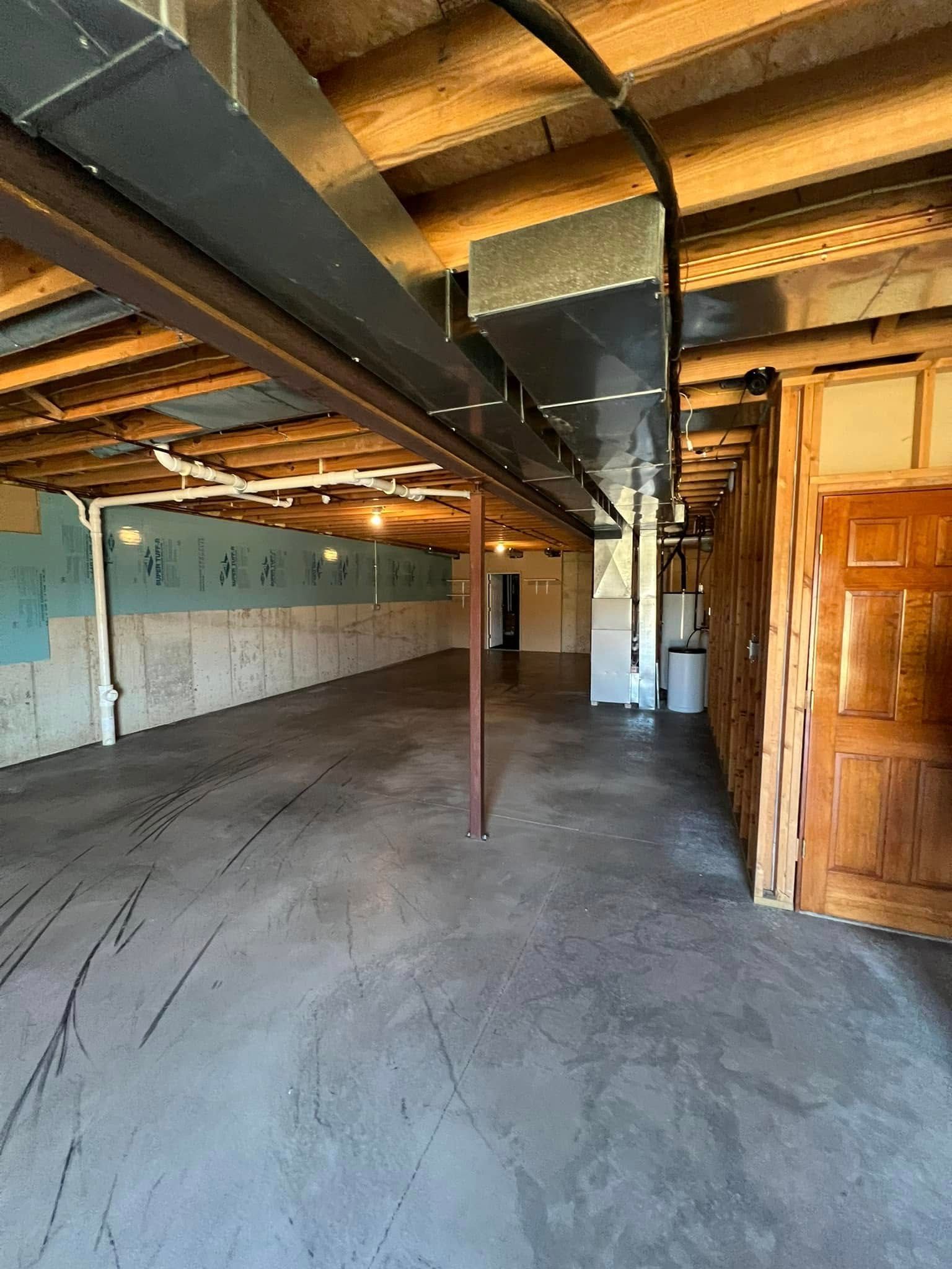 Basement interior with exposed beams, ductwork, and concrete floor. Walls are partially painted.