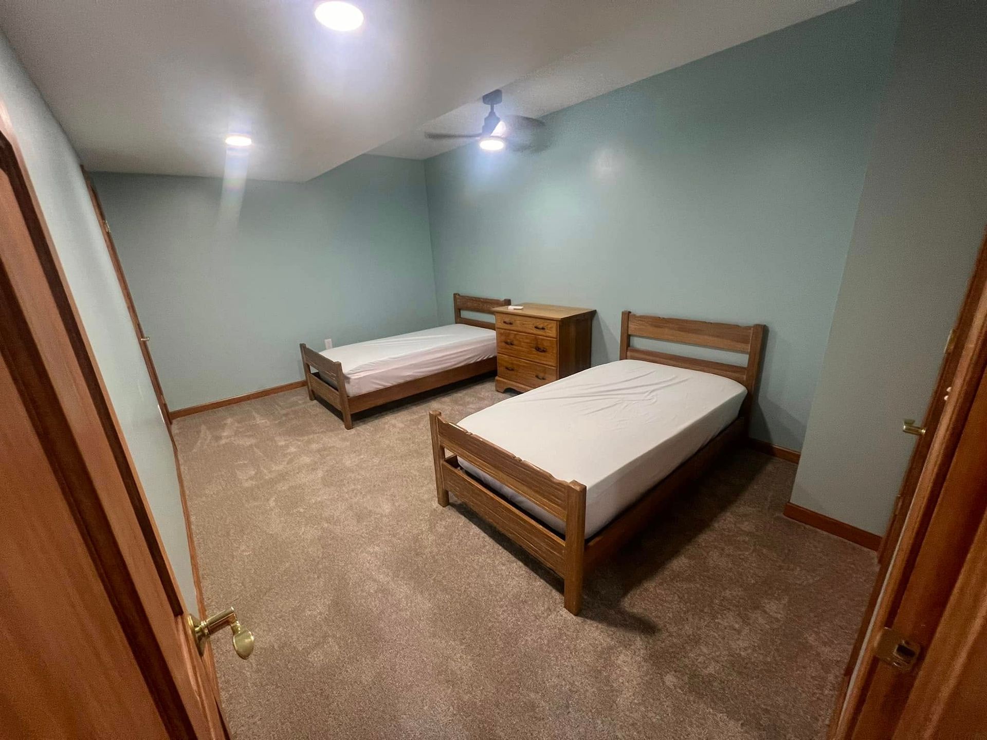 Two twin beds in a room with light blue walls and wood trim, carpeted floor.