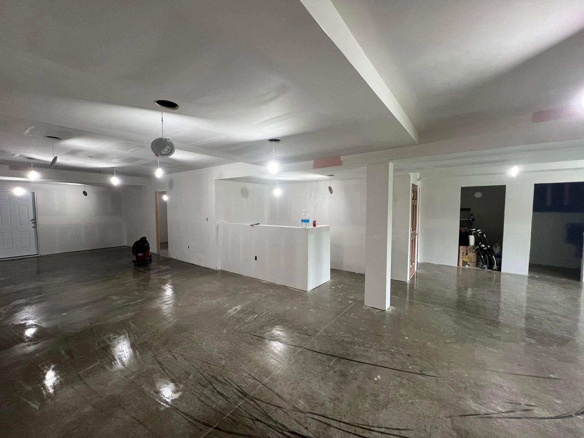A bare room under construction with a concrete floor, white walls, and exposed light fixtures.