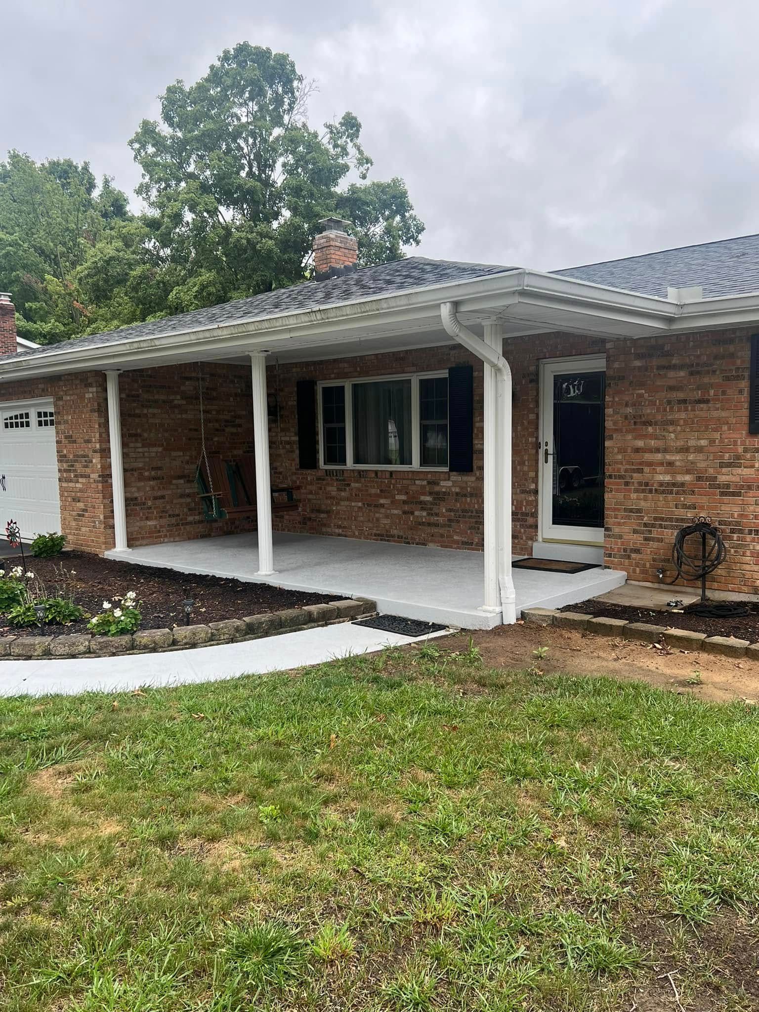 Brick house with a covered porch and white columns. Green grass and cloudy sky.