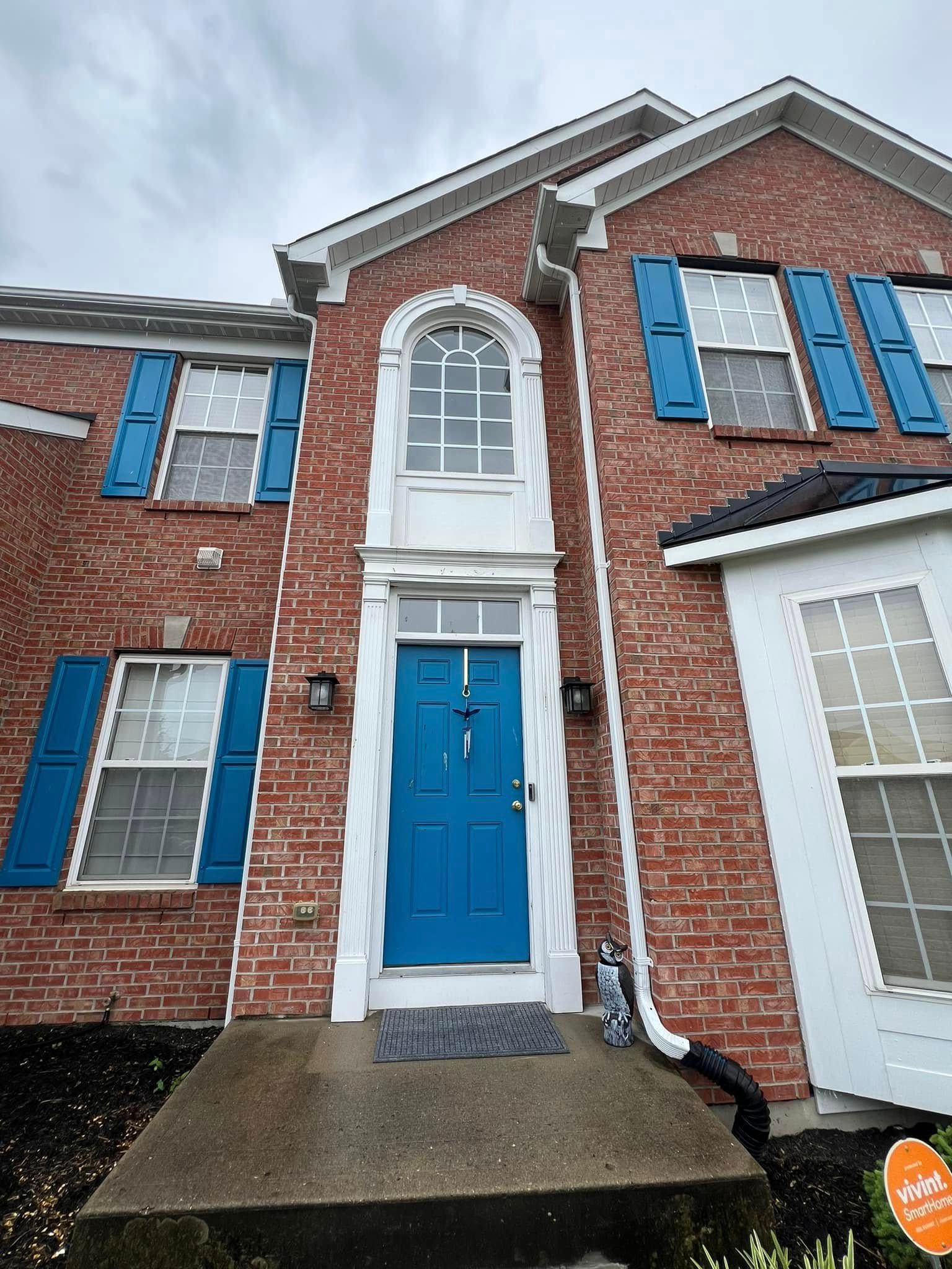 Red brick house with blue door, shutters, and white trim. Overcast sky.