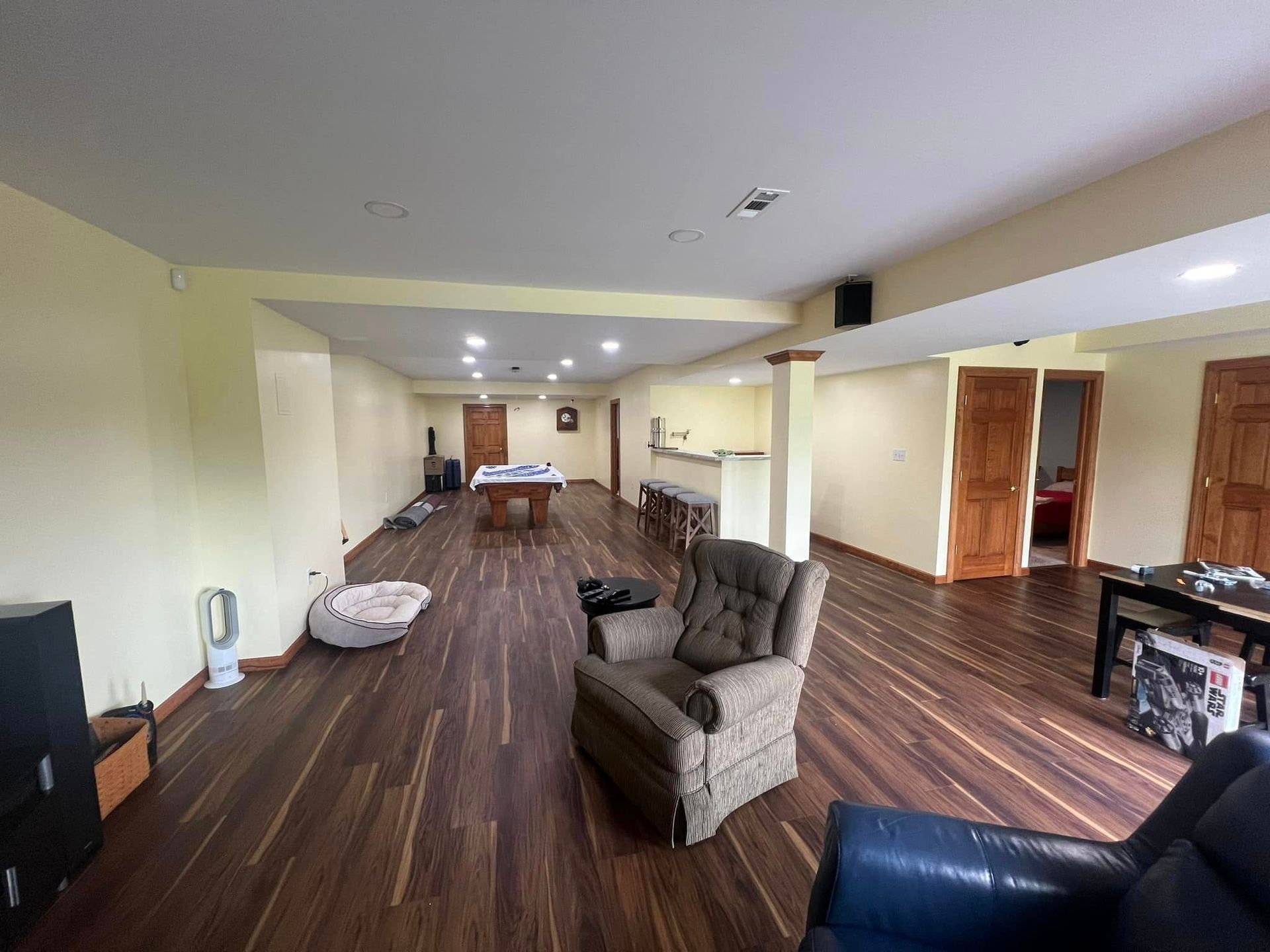 Spacious basement with hardwood floors, a pool table, and seating. Light yellow walls and brown doors.