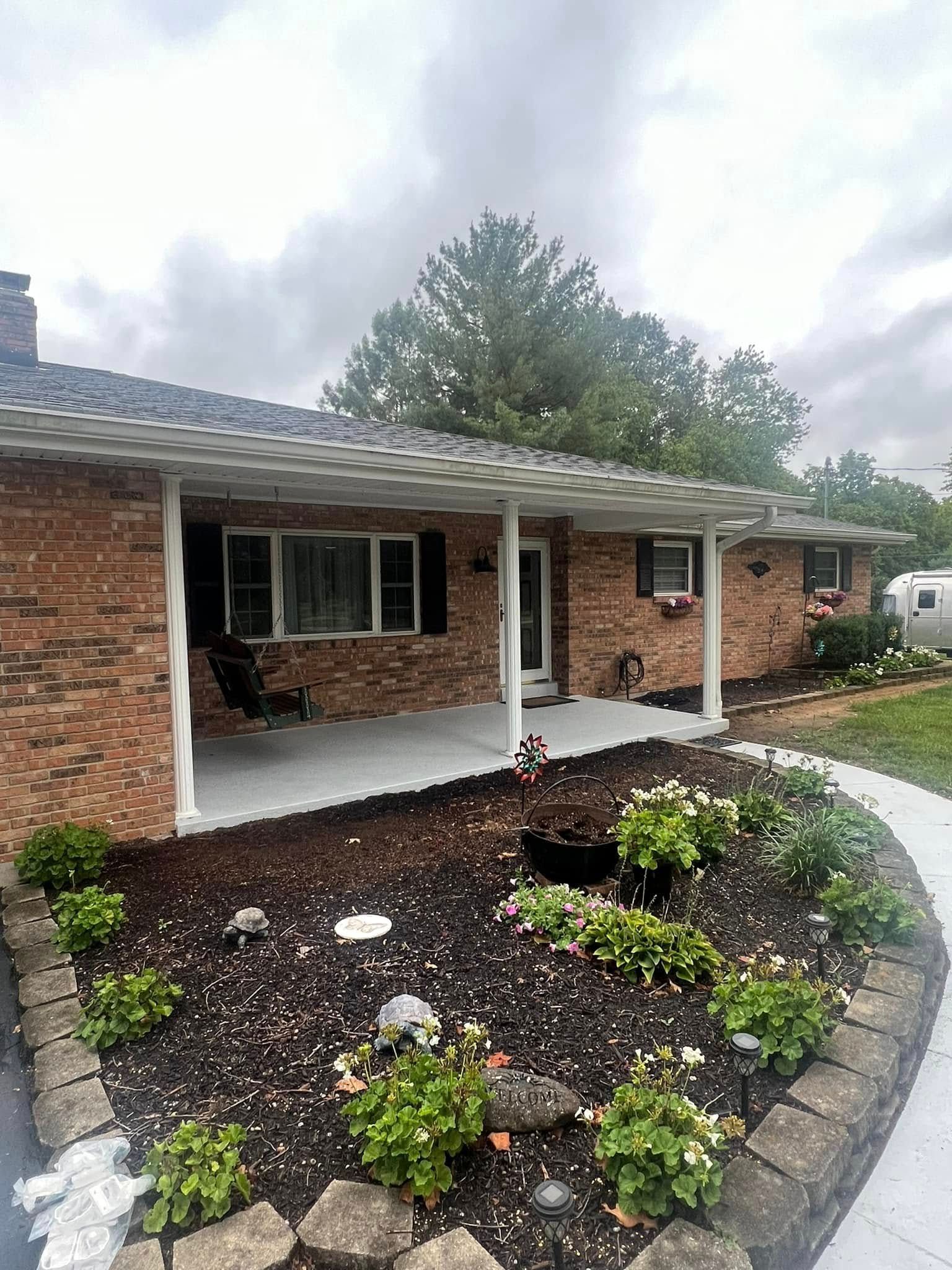 Brick house with a covered porch, flower bed, and a cloudy sky.