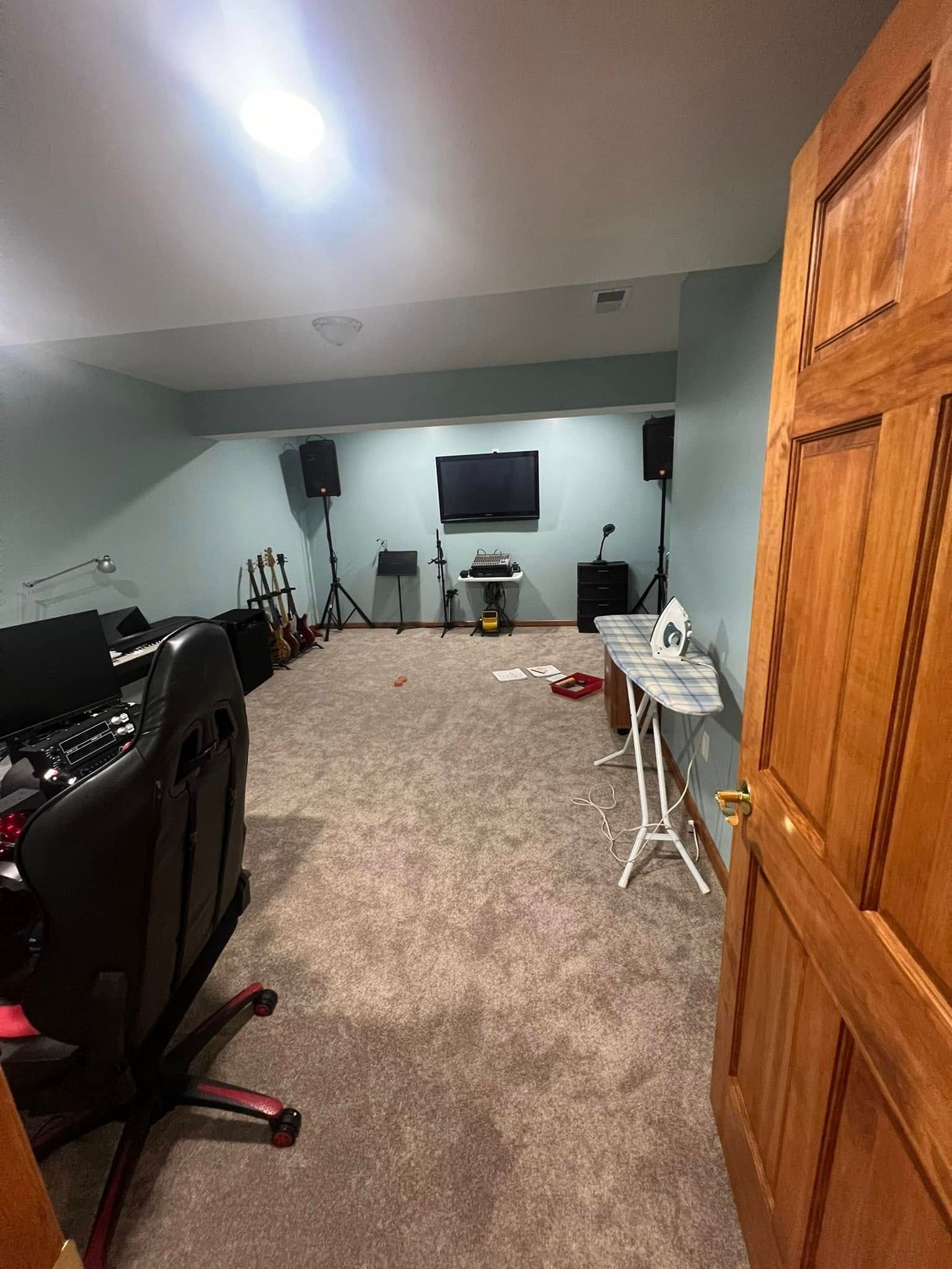 A room with a TV, speakers, a mixing console, and an ironing board.