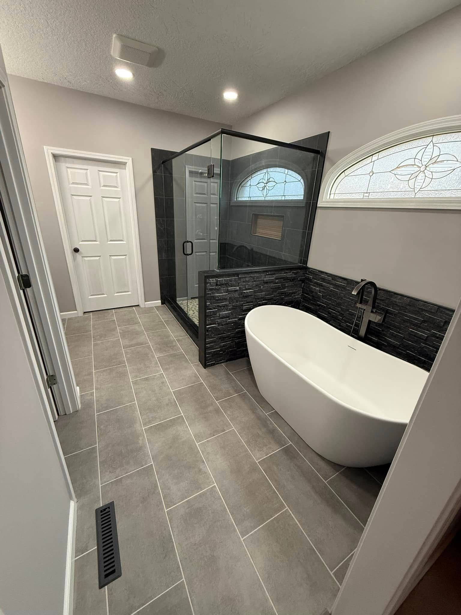 Modern bathroom with gray tiled floor, a freestanding white tub, and a black-framed glass shower.