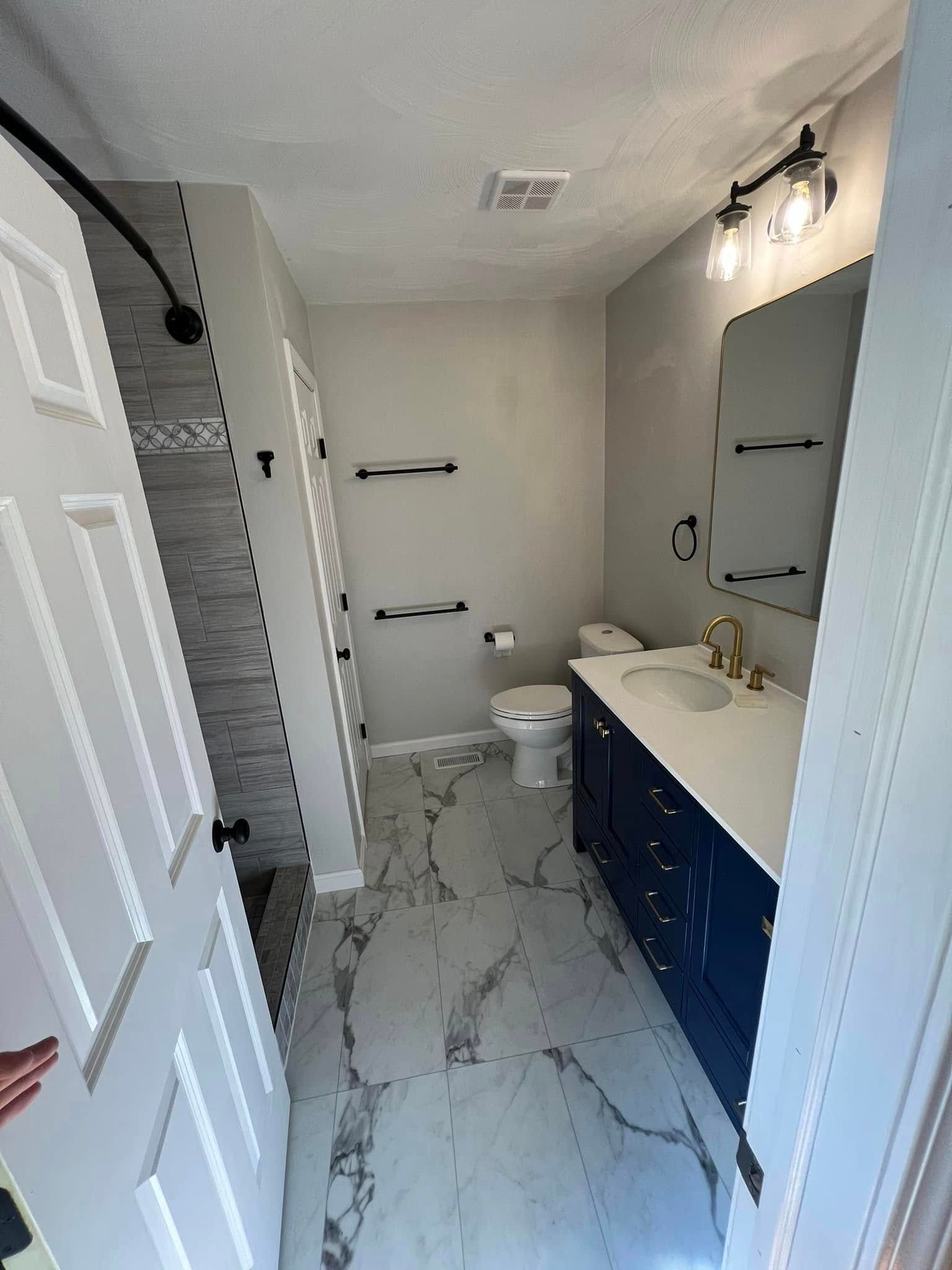 Newly remodeled bathroom with navy vanity, white countertop, and gray and white tile floor.