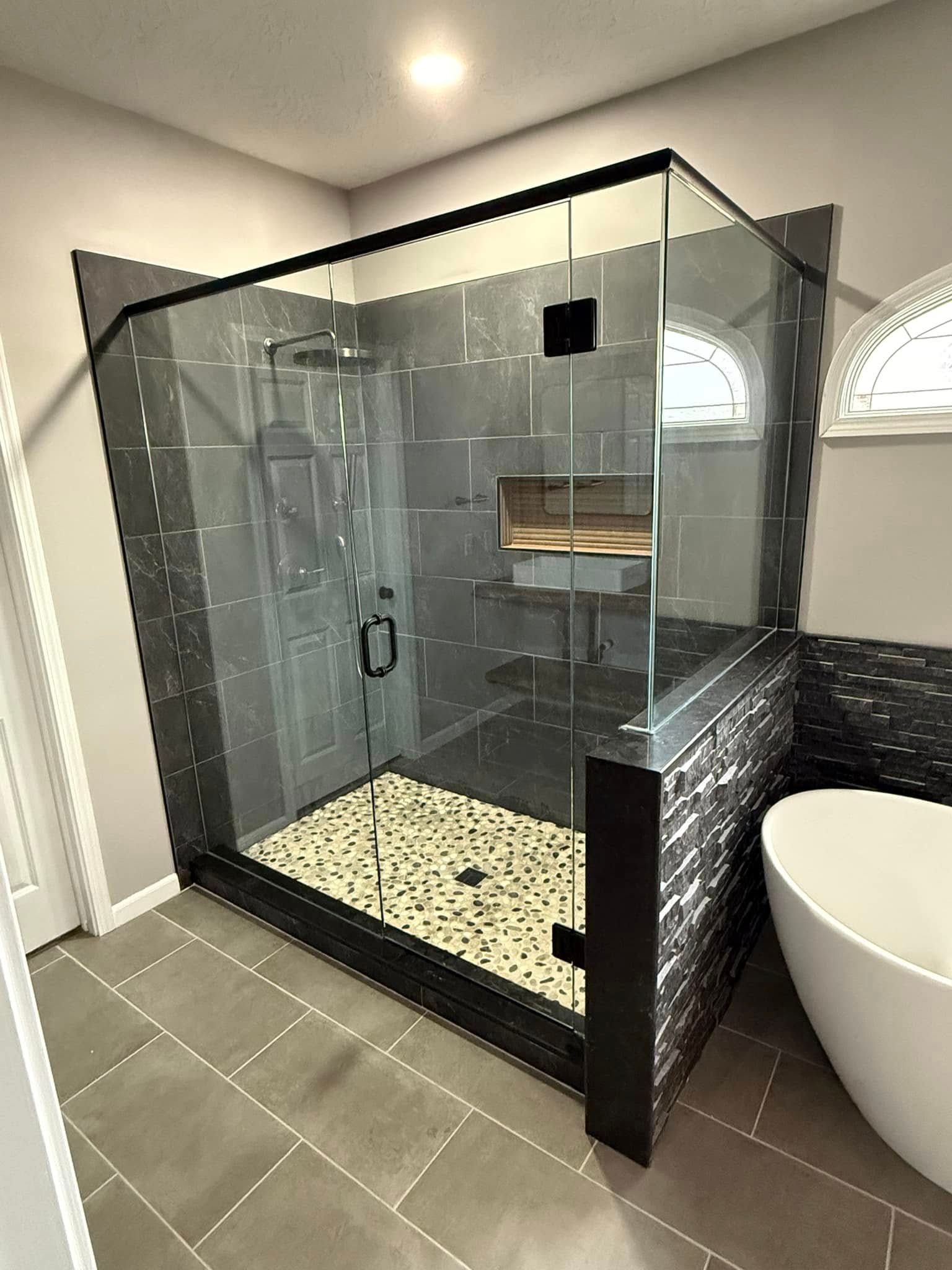Modern bathroom with glass shower enclosure, gray tile, and a soaking tub.
