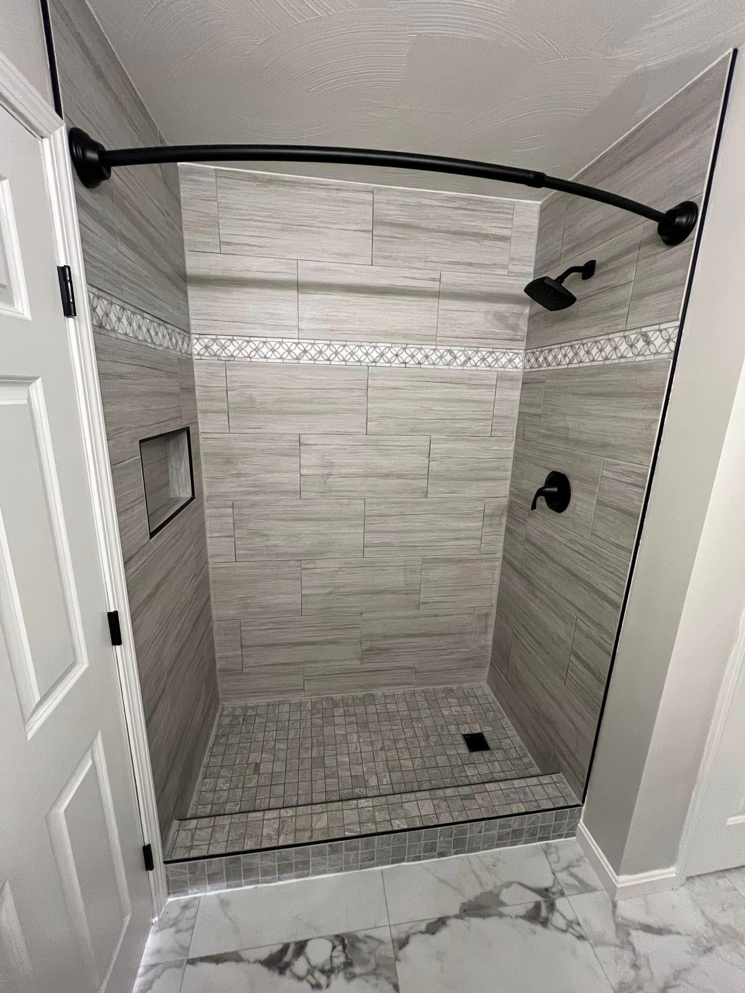 Bathroom with gray stone-like tiles, curved shower rod, and black fixtures.