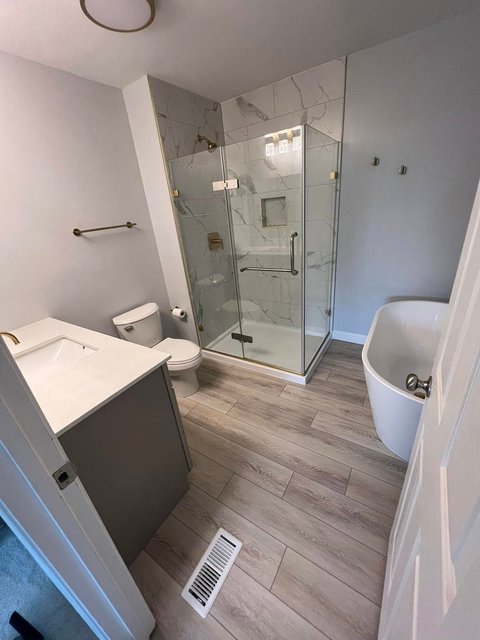 Modern bathroom with glass shower, freestanding tub, gray vanity, and light wood-look tile.