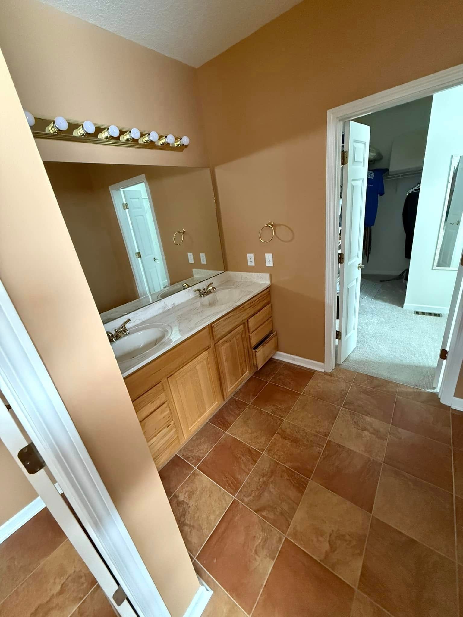 Bathroom with tan walls, brown tile floor, and a wooden vanity. A closet is in an open doorway.
